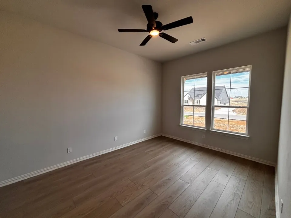 Spacious room featuring wood-finish flooring, two large windows, a ceiling fan with integrated lighting, and neutral wall tones