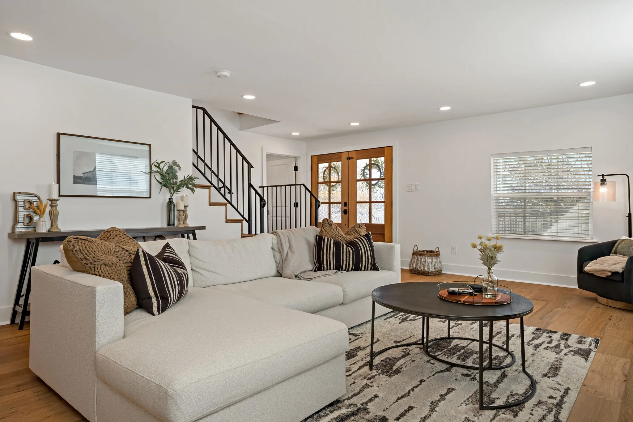 Recessed lighting, wood flooring, white walls, black metal staircase railing, and wood double doors with frosted glass