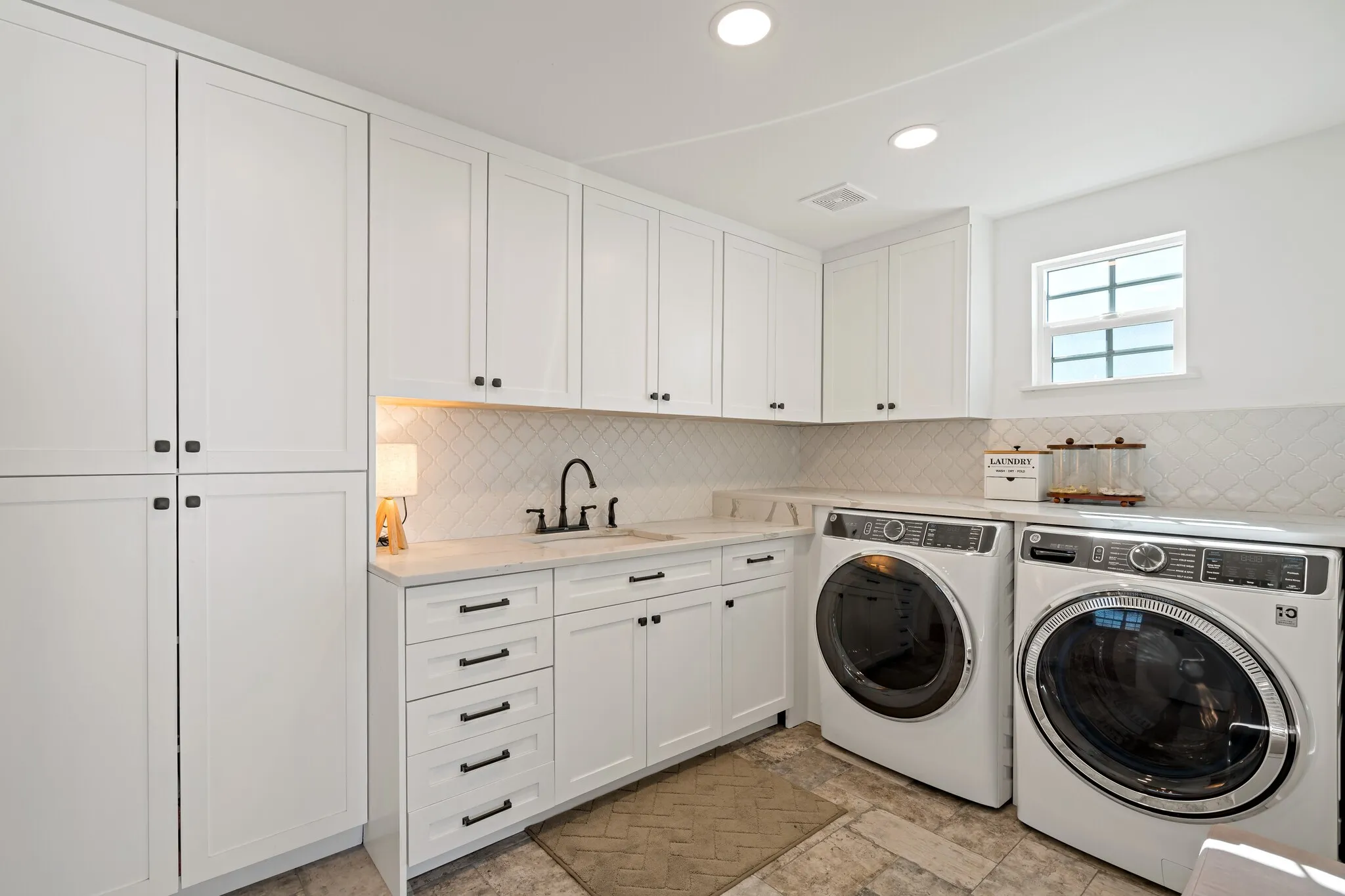 White shaker cabinetry, light-toned countertop, sink with matte black faucet, geometric pattern backsplash, and recessed lighting