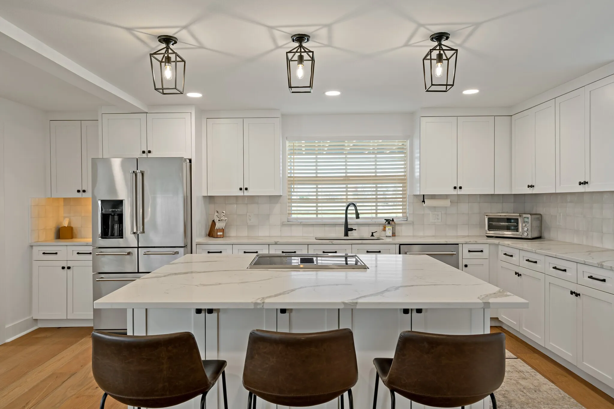 Kitchen featuring white cabinetry, a large kitchen island with a cooktop, quartz countertops, stainless steel appliances, and wood flooring