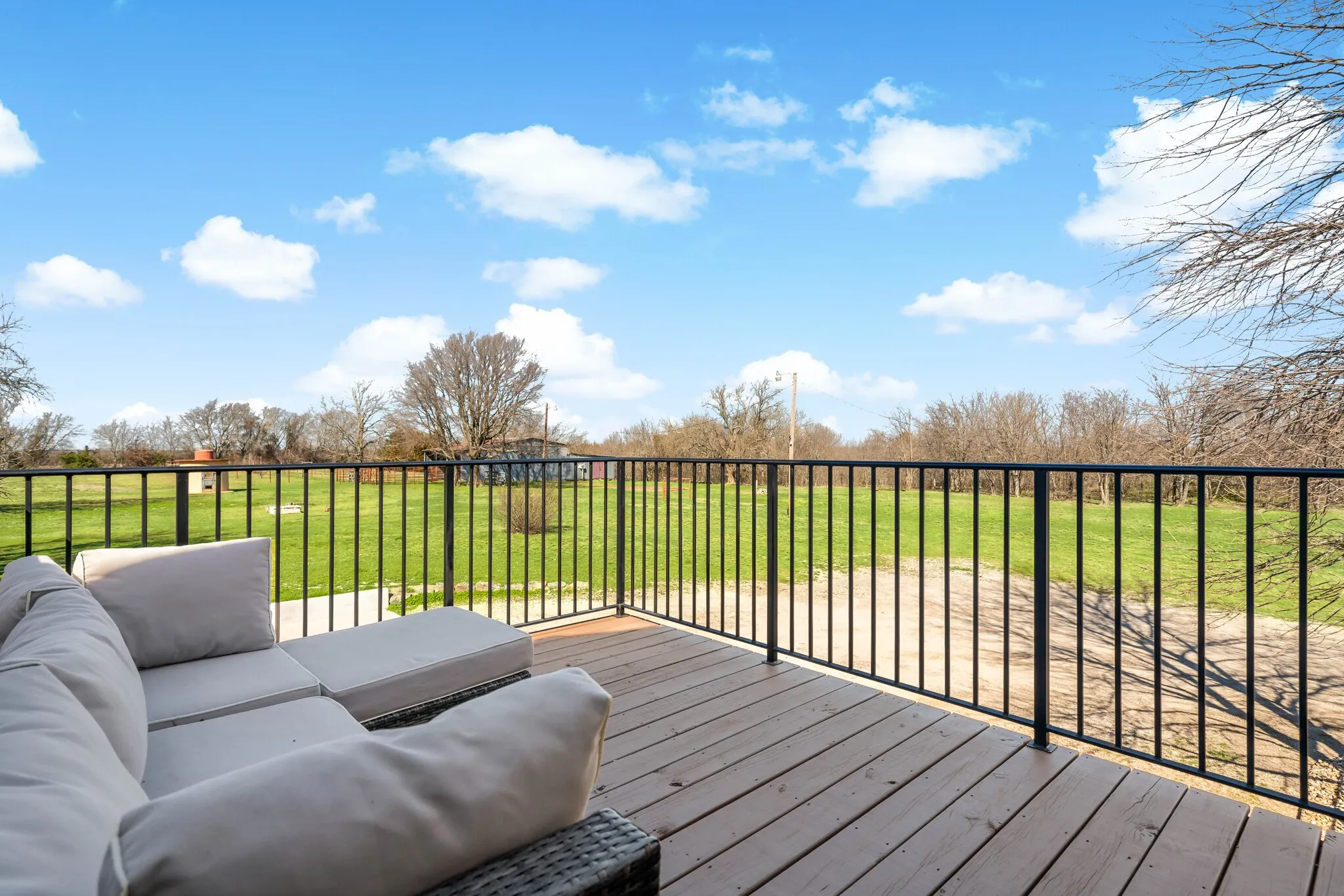 Deck with wood-finish flooring and black metal railings, overlooking a large green outdoor area
