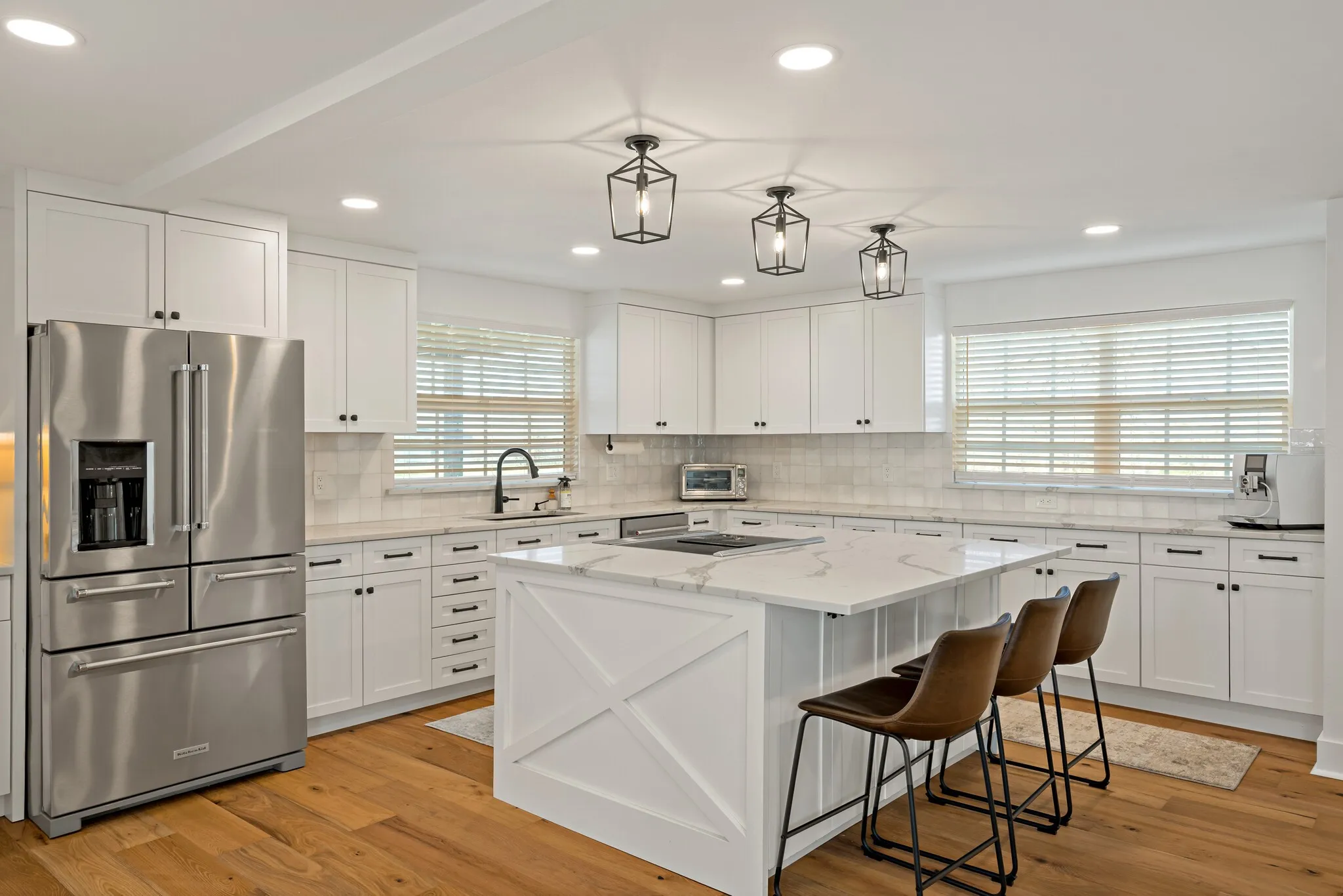Chef's kitchen featuring custom white cabinetry with hardware accents, quartz countertops, a large center island with seating for three, pendant lighting, and wood flooring throughout