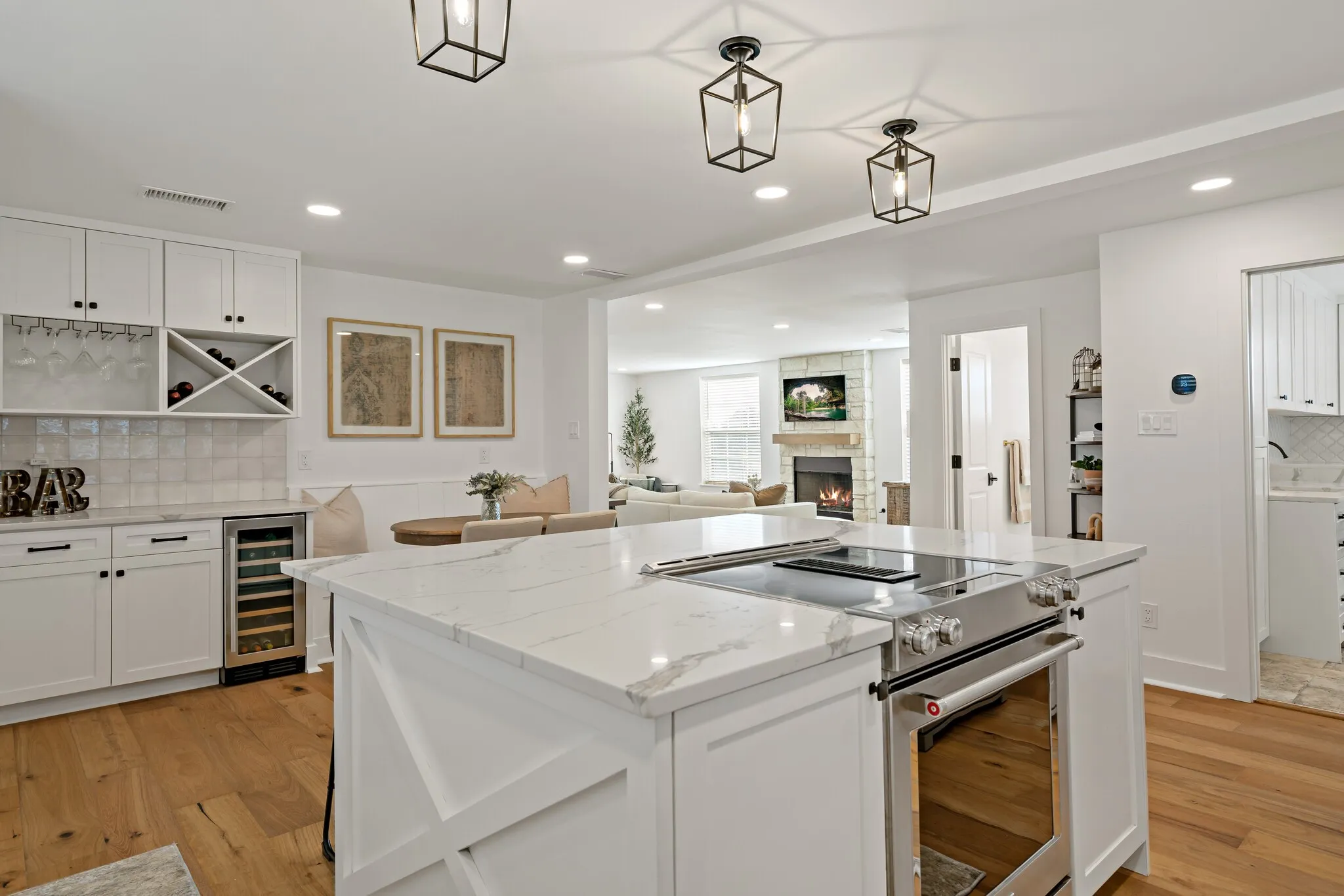 Gourmet kitchen showcasing white cabinetry with X-panel detailing, a large island with prep space, stainless steel range, white quartzite  countertops, recessed and pendant lighting, hardwood flooring, and an open layout connecting to adjacent living spaces