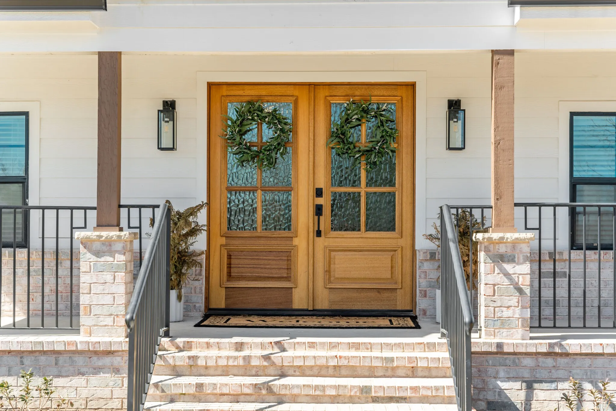 Double wood entry doors with textured glass panels,black wrought iron railing, and exterior wall sconces