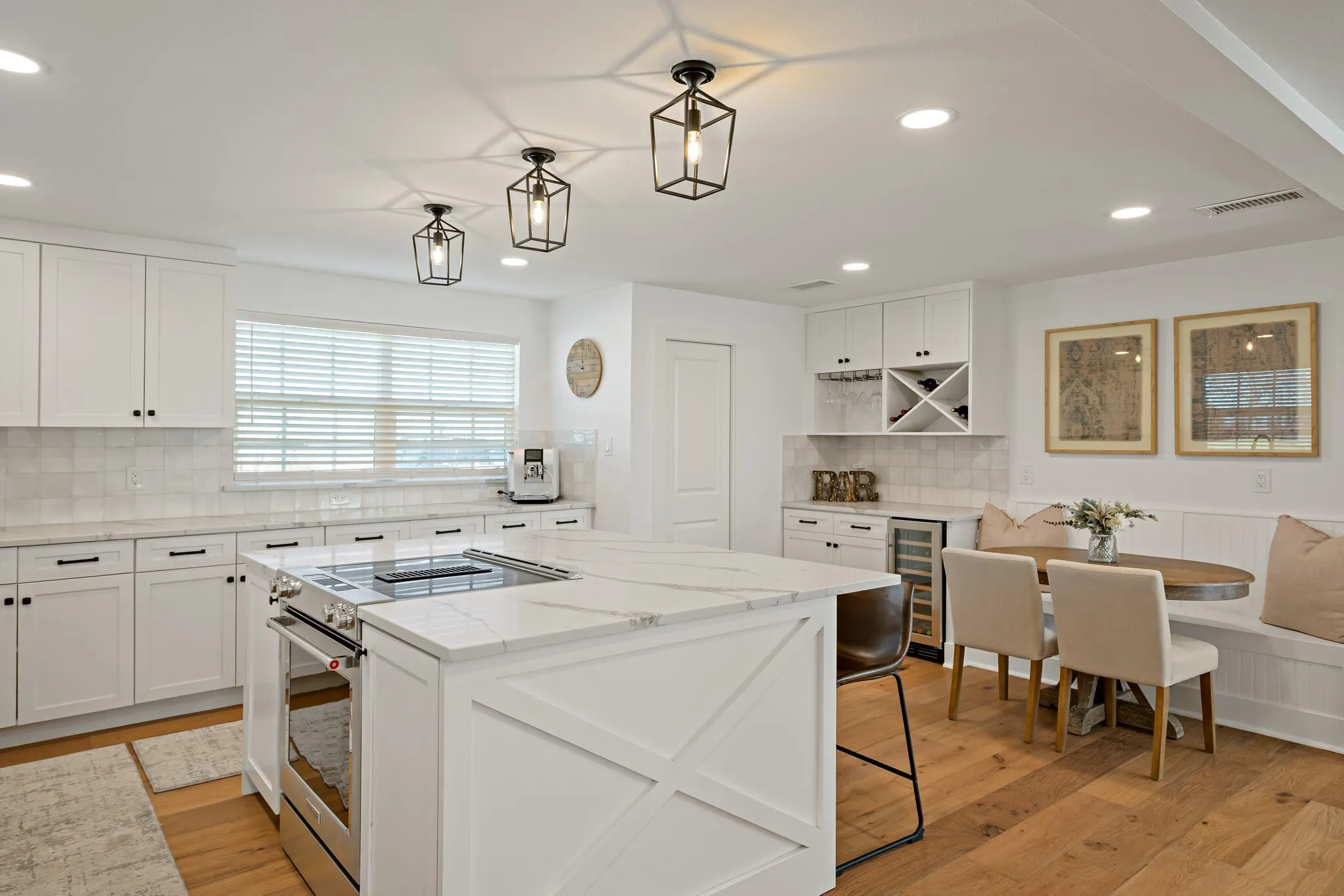 Open-concept kitchen featuring a large central island with a cooktop, white shaker cabinetry, quartz countertops, and wood  flooring
