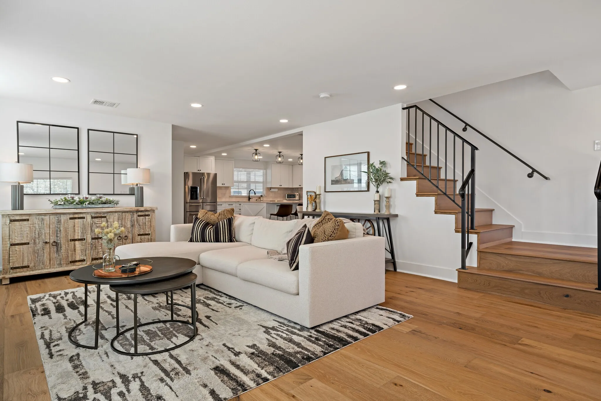 Recessed lighting, wood flooring, staircase with dark iron railing, open-concept layout, and kitchen with stainless steel appliances