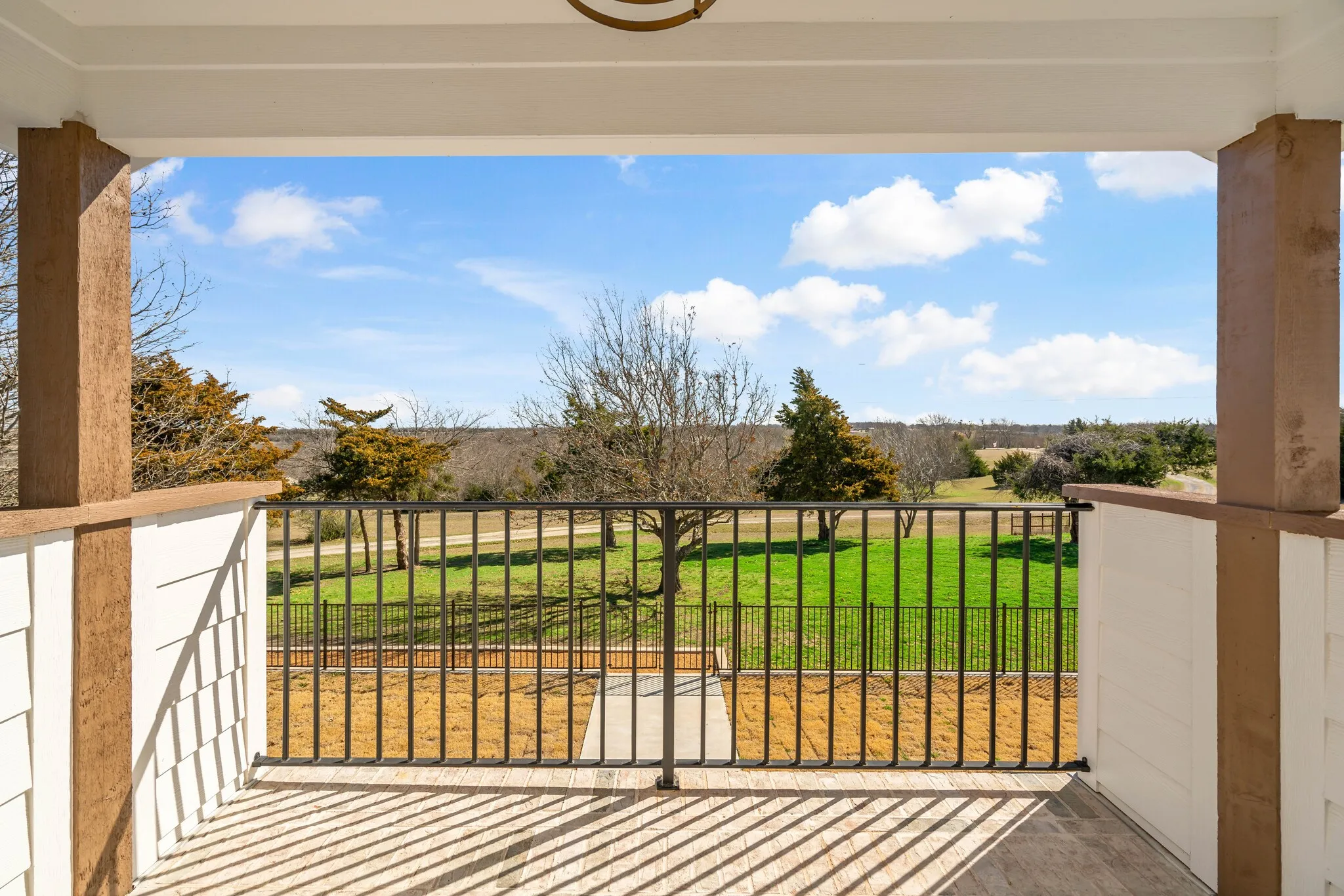 Covered patio with a metal railing and tile flooring, opening to an expansive outdoor area