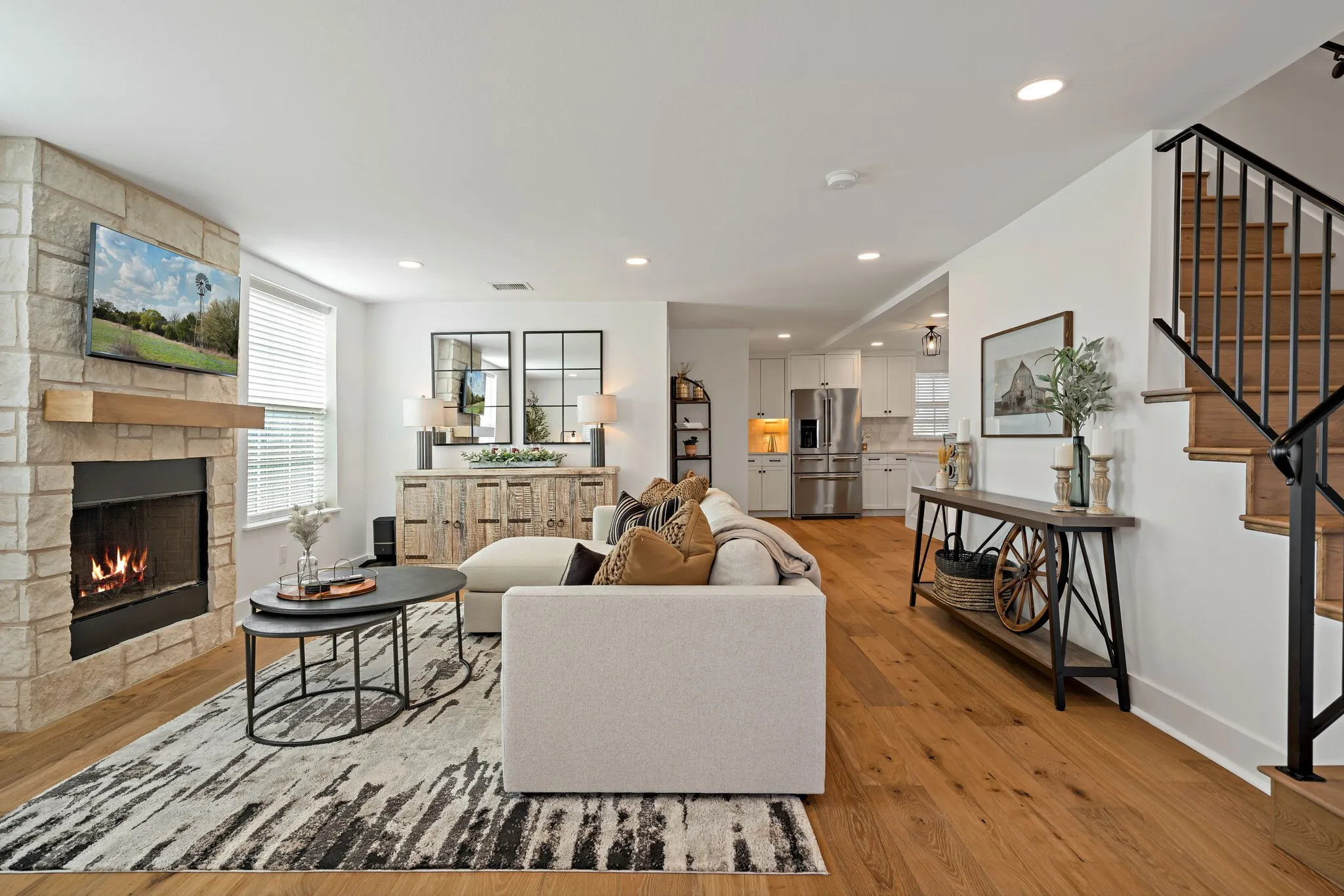Open-concept living area featuring hardwood flooring, fireplace with stone surround, recessed ceiling lighting, and opens to the kitchen and dining area.