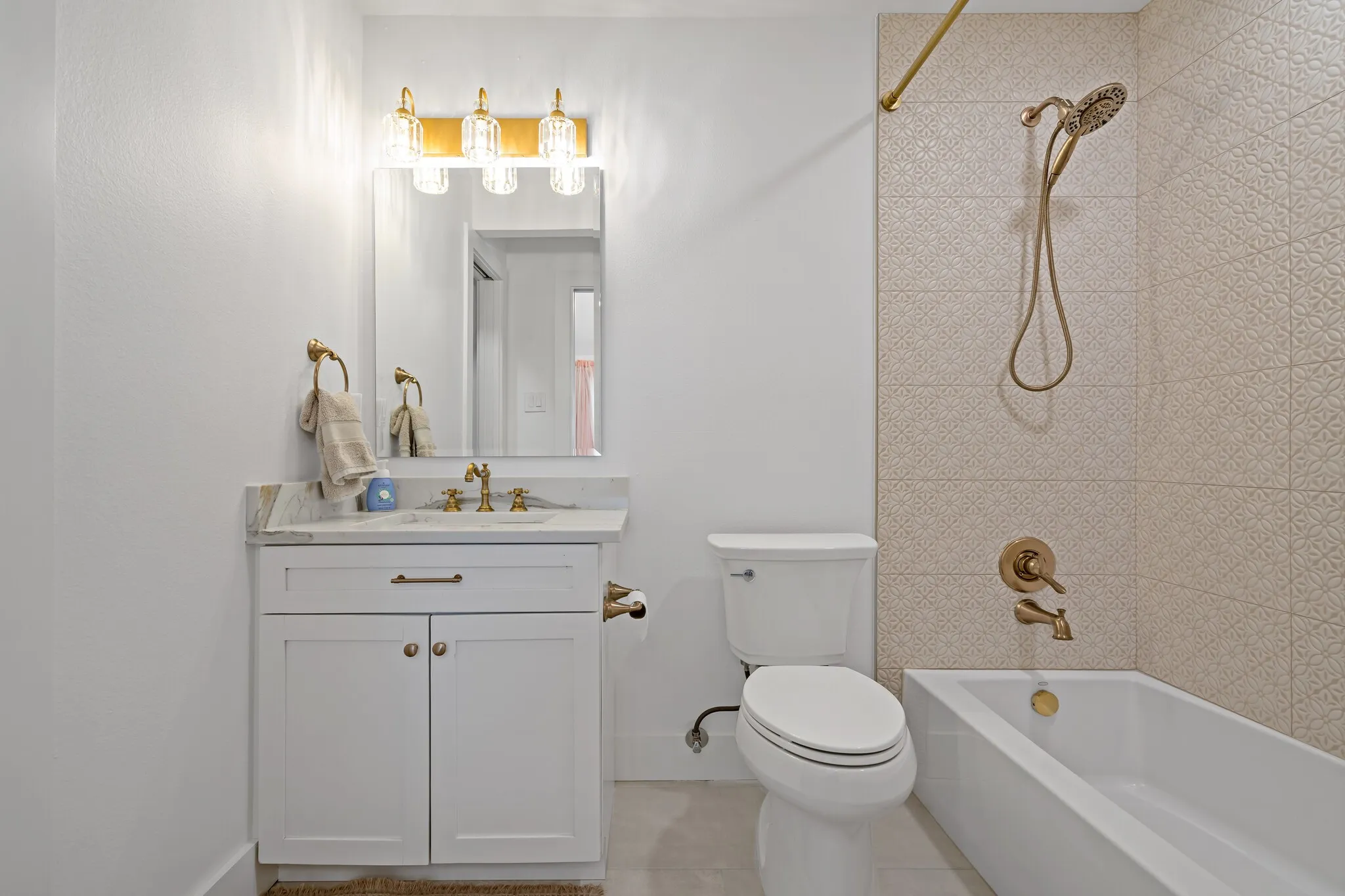 White vanity with a stone countertop, mounted mirror, and gold-finish fixtures