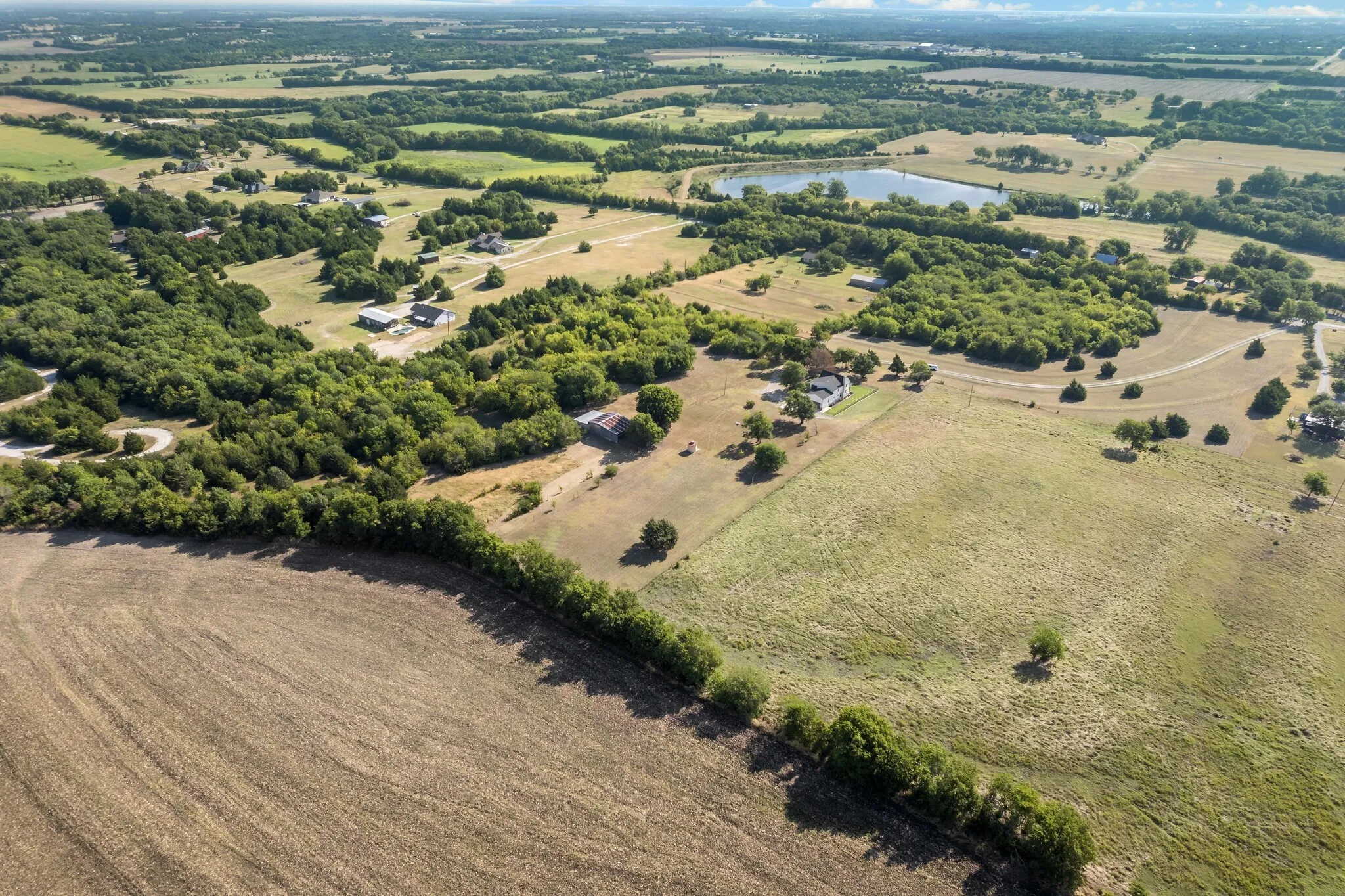 Expansive land parcel featuring open fields, scattered trees, and a distant natural pond