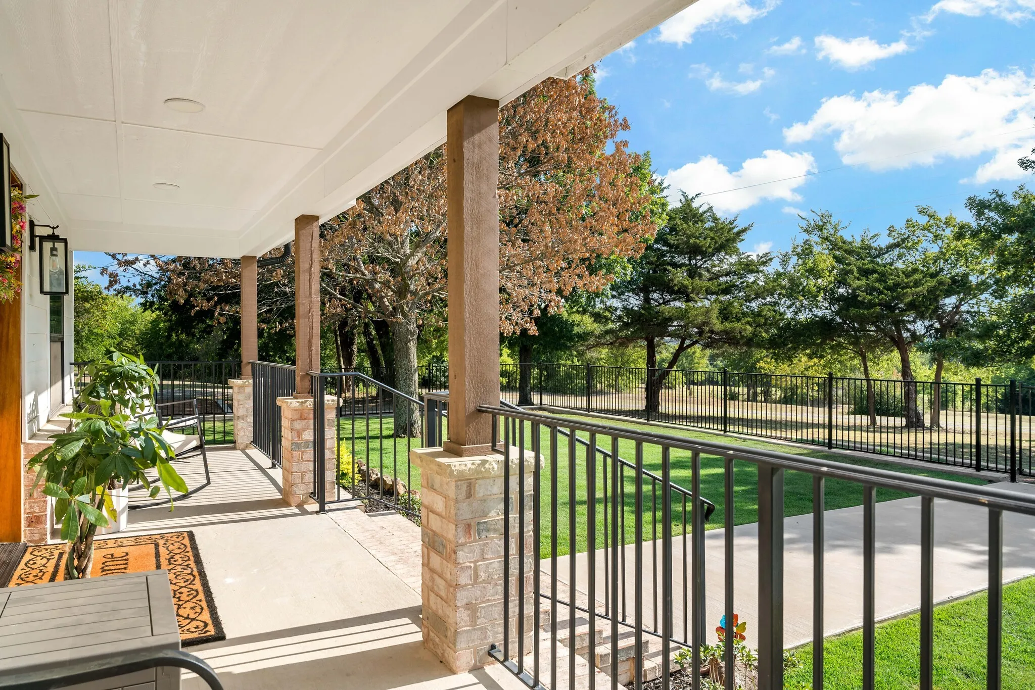 Covered front porch featuring wood columns, brick accents, and a concrete surface.
