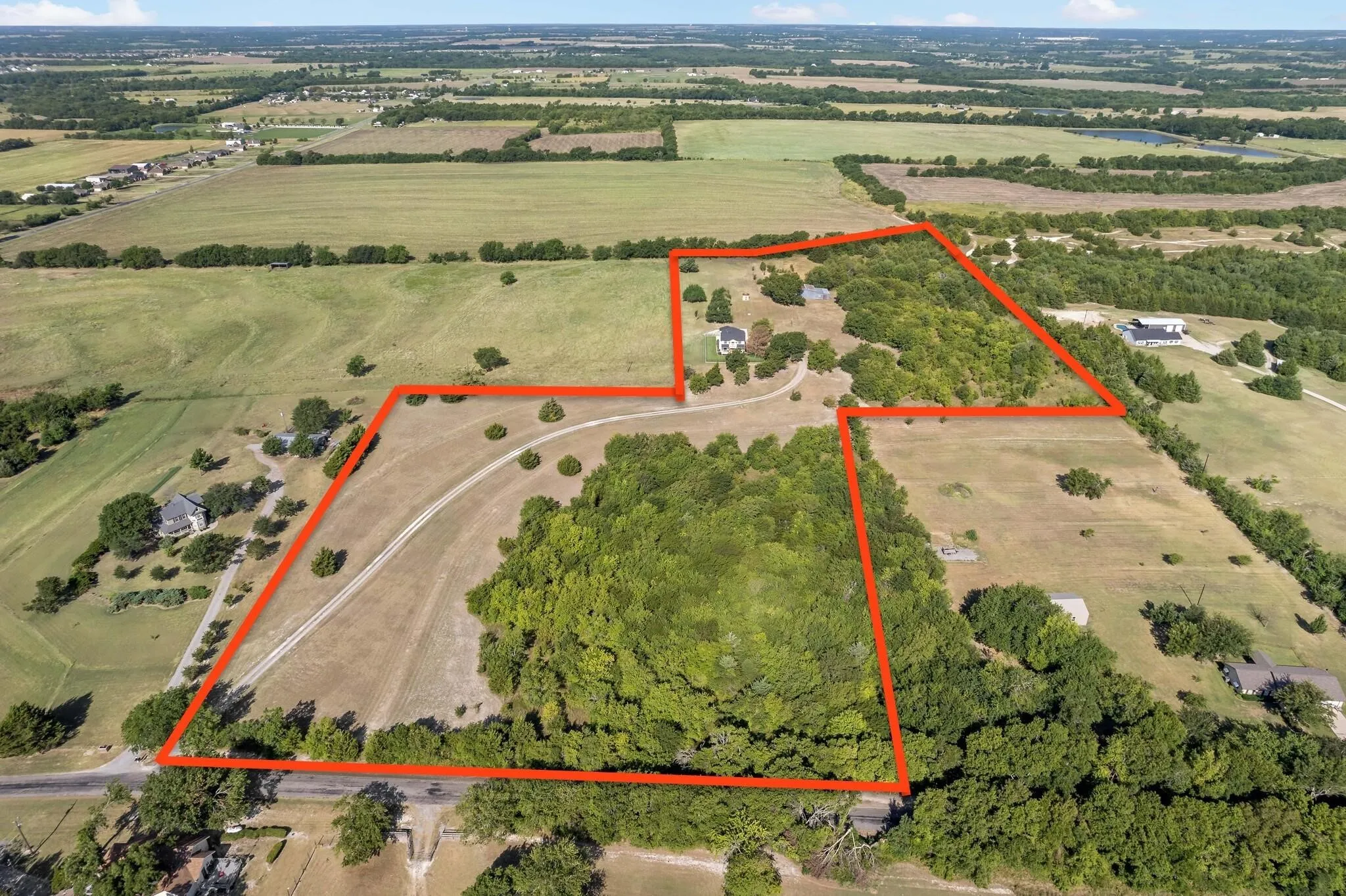 Expansive land parcel featuring open fields, wooded areas, a winding dirt road, and a distant structure