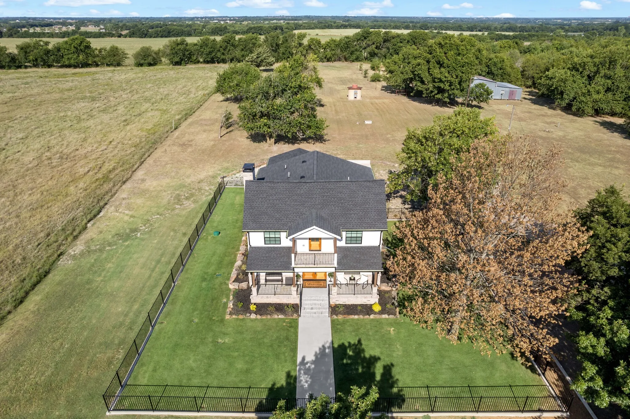 Stately two-story residence set on expansive grounds featuring a dark architectural shingle roof, white exterior trim, and a centered front entry with covered portico