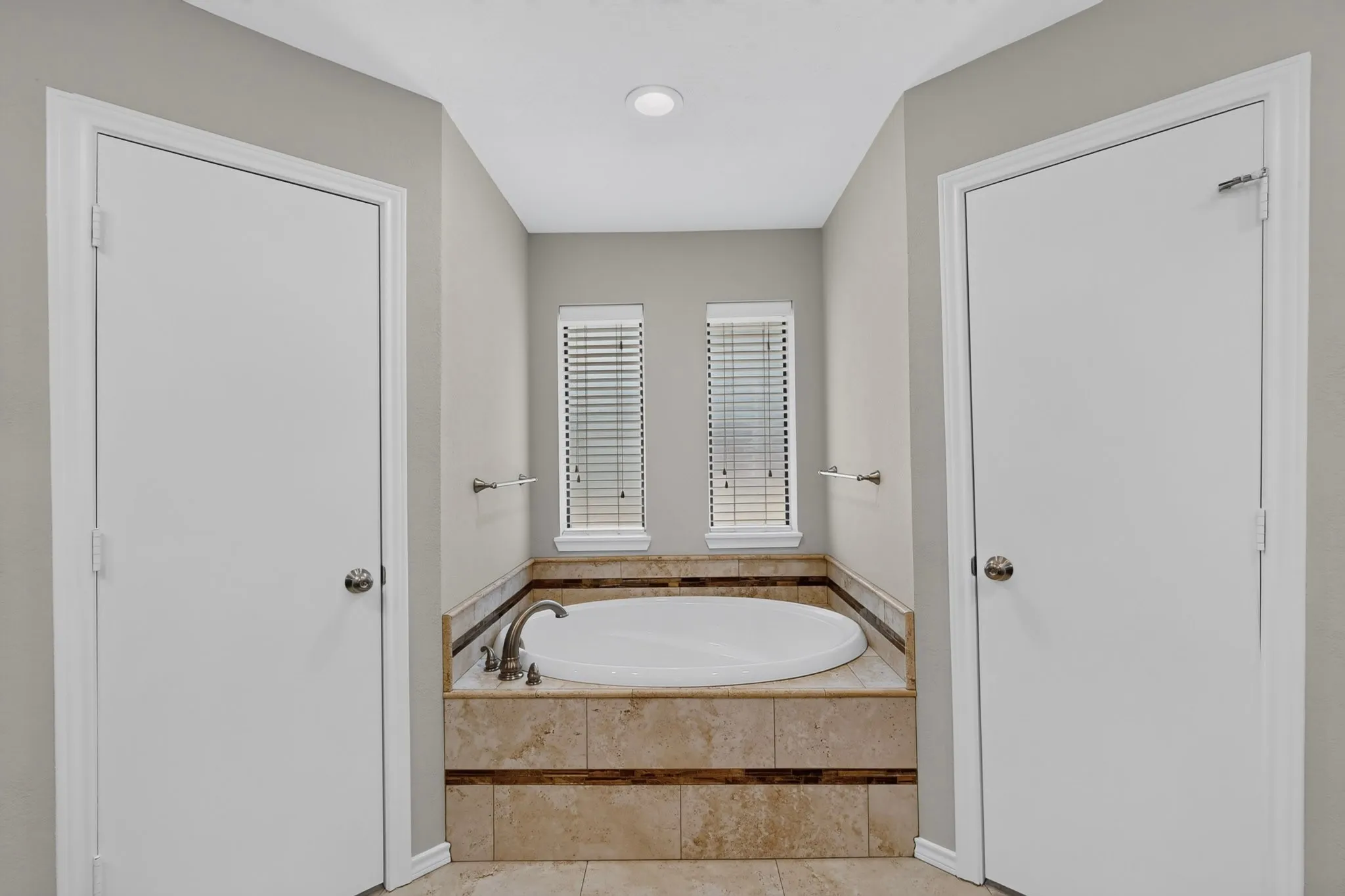 Primary Bathroom featuring a sunken soaking tub with wood-finish surround, dual operable windows with plantation shutters, recessed ceiling lighting, and dual white panel doors flanking the spa-inspired layout