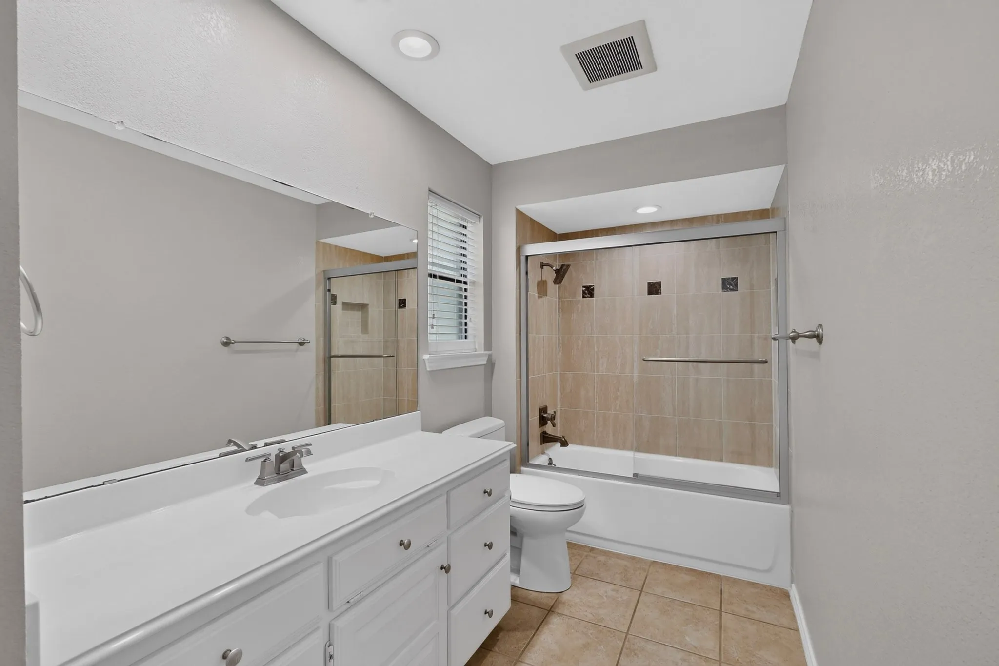 Bathroom featuring a single vanity, large mirror, and tiled shower/tub combination with a sliding glass door