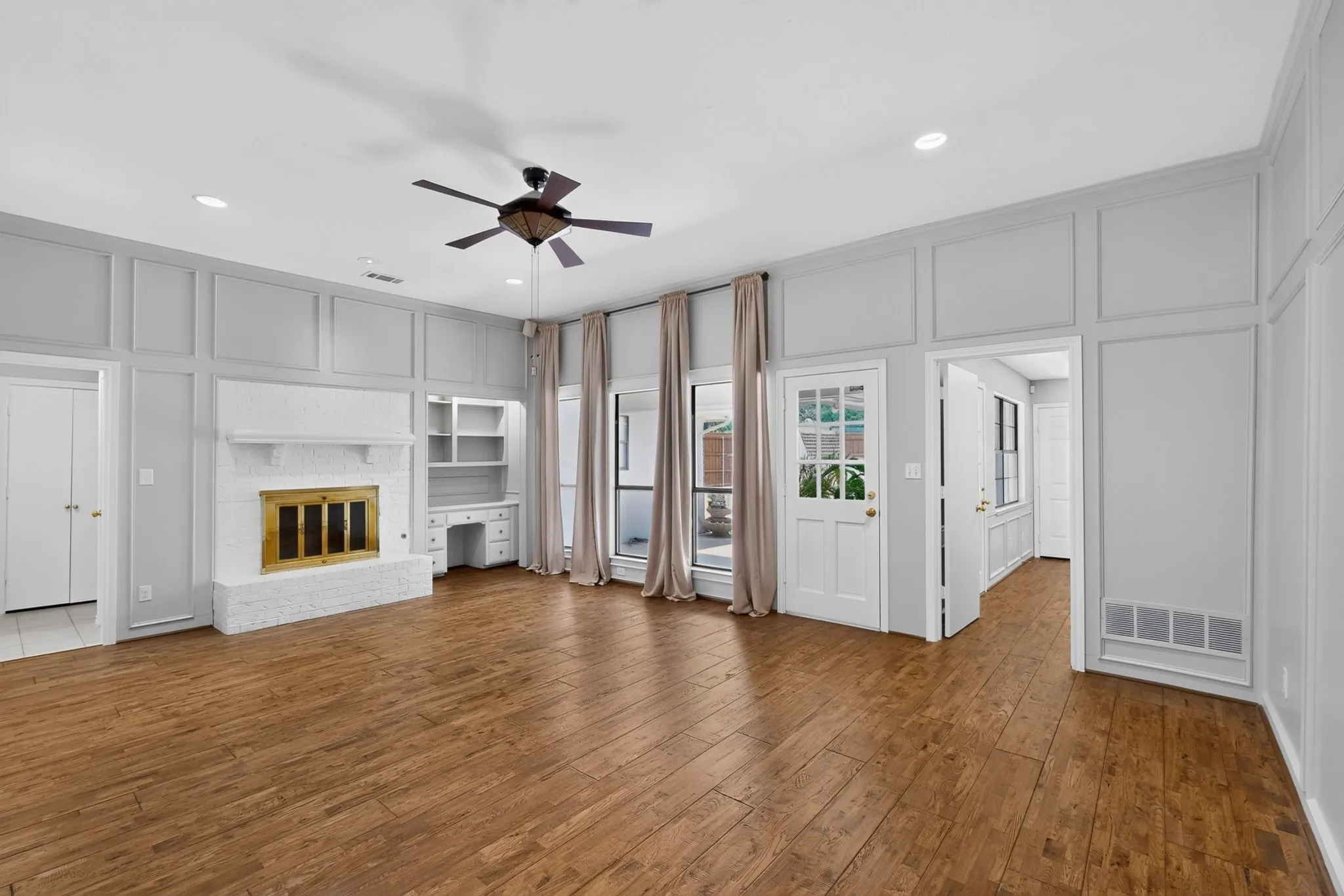 Spacious primary living area showcasing rich wood-finish flooring, coffered ceiling detail, and abundant natural light from multiple French doors and transom windows