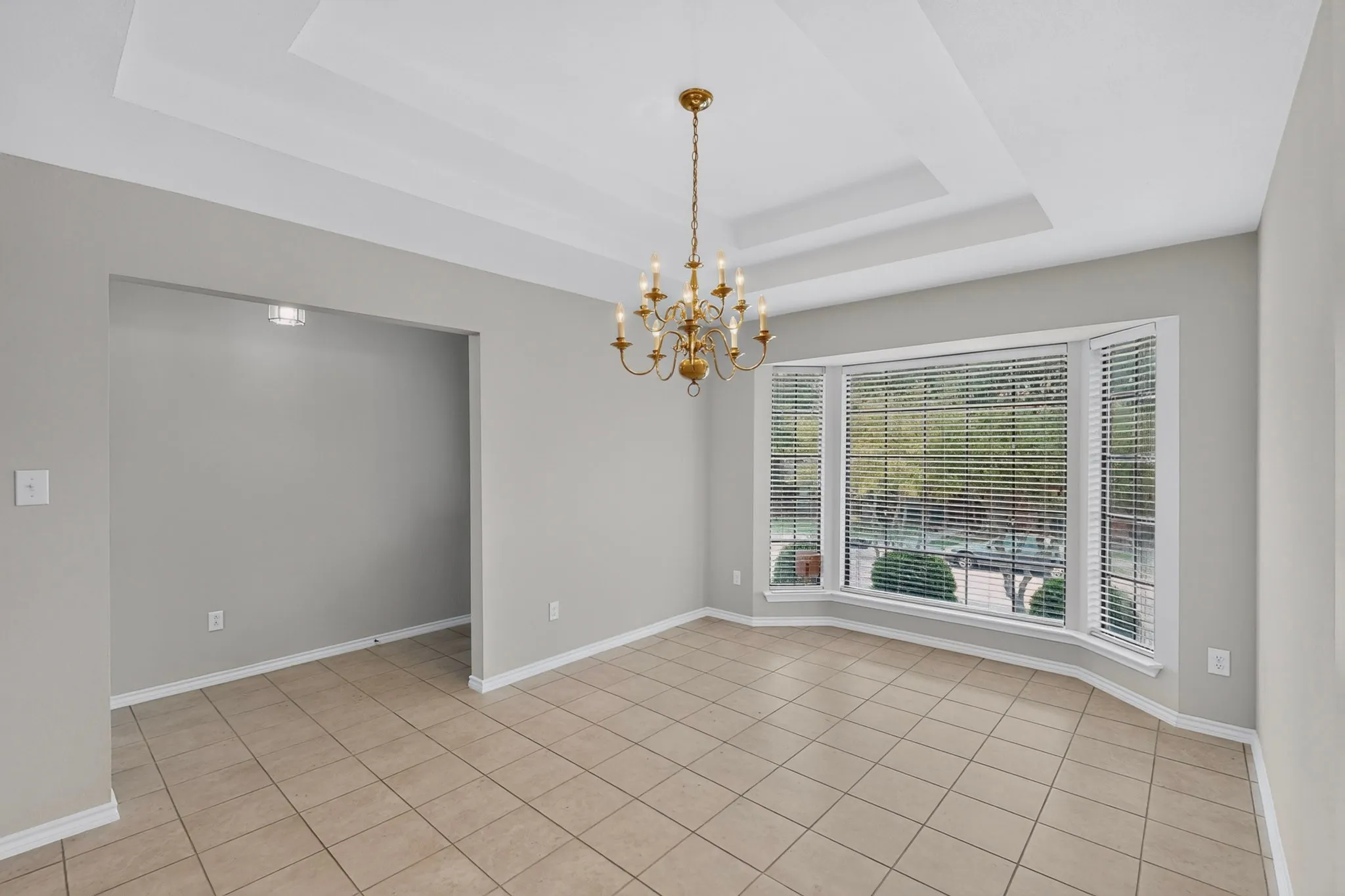 Bright and spacious dining area featuring neutral wall finishes, tile flooring, coffered ceiling detail, and a decorative brass chandelier