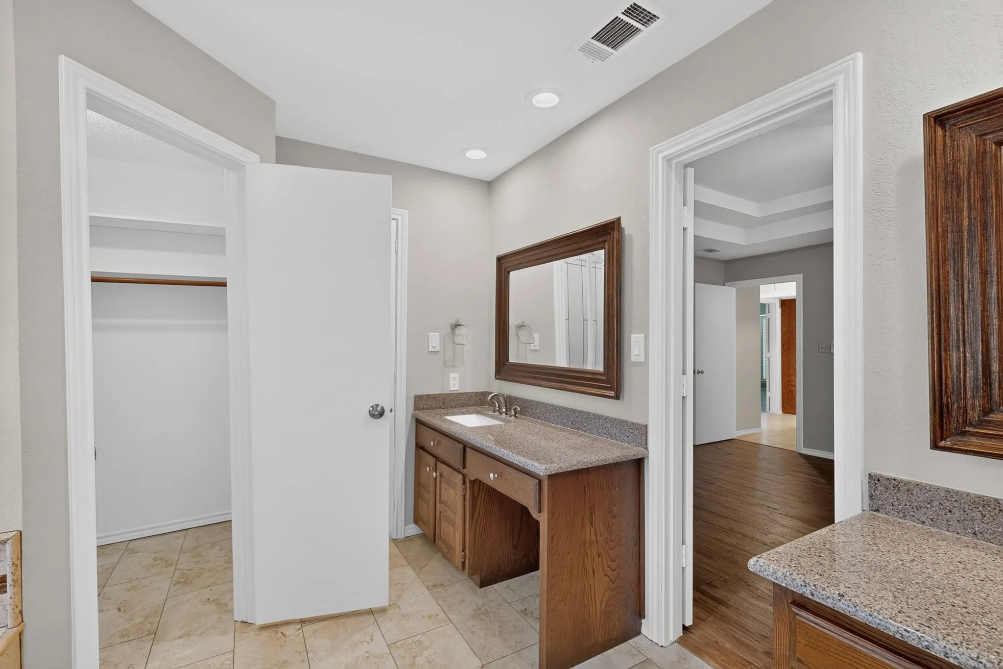 Spa-inspired primary bathroom featuring dual vanities with stone countertops, wood cabinetry, and framed mirror