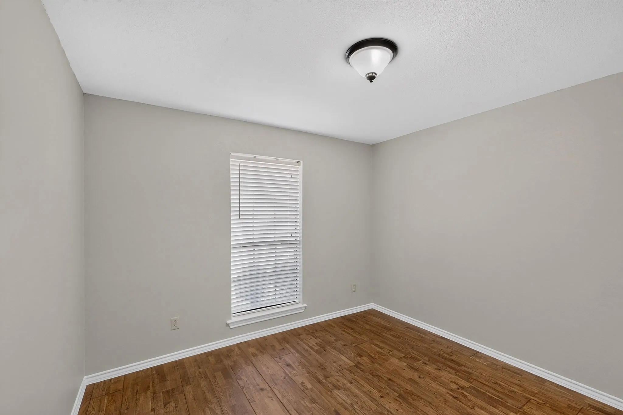 Wood-finish flooring, neutral wall paint, and a single window with blinds