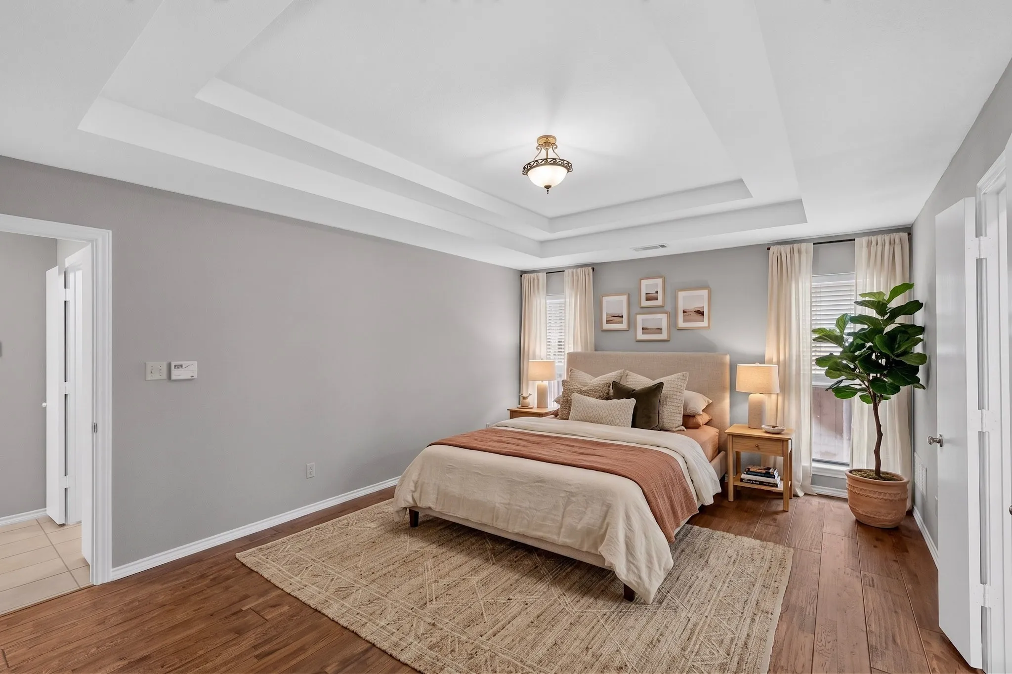 Tray ceiling with a decorative light fixture, wood-finish flooring, and white window blinds