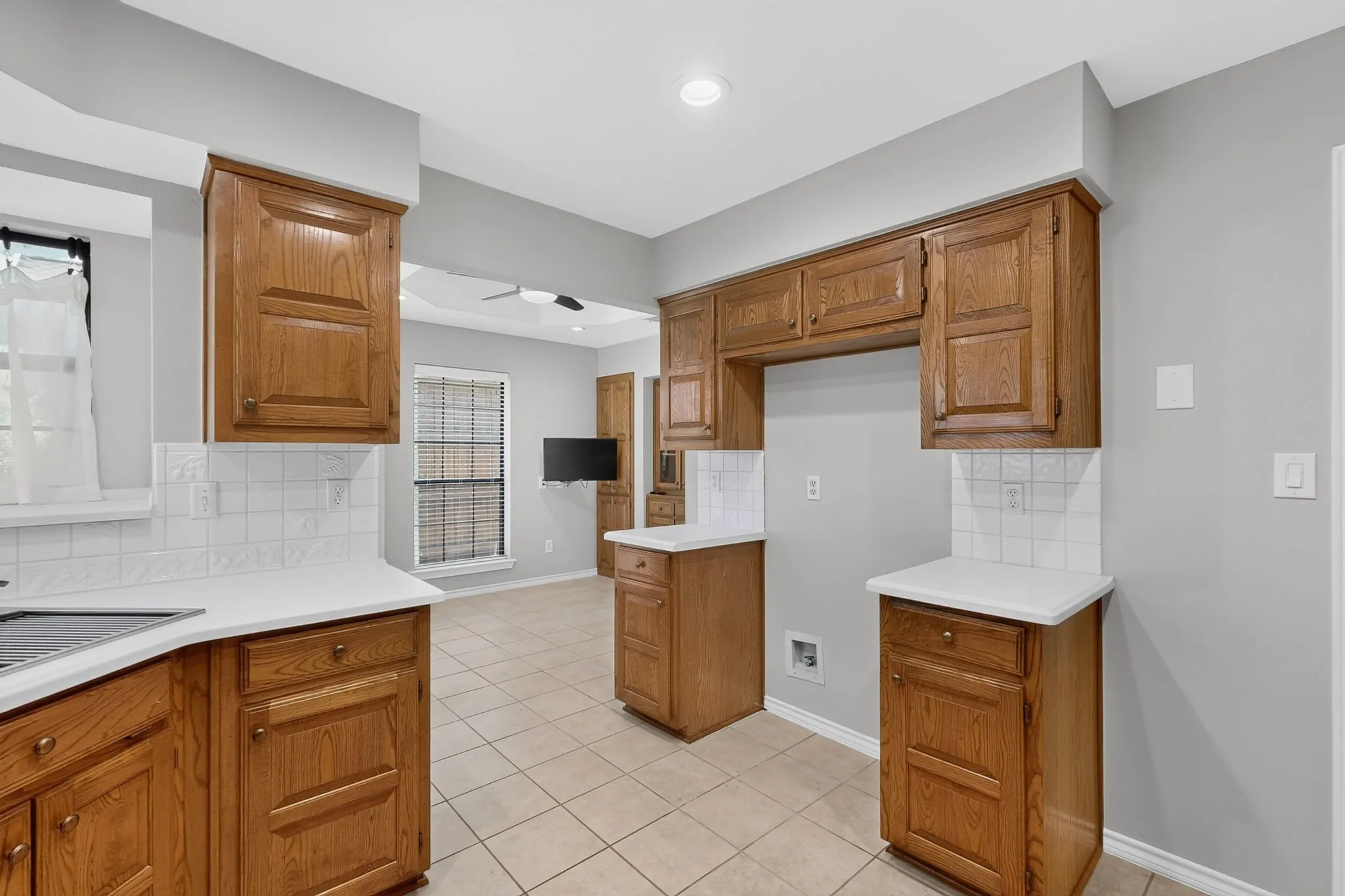 Spacious kitchen featuring warm wood cabinetry with raised-panel doors, white subway tile backsplash, white countertops, a central island with dedicated workspace, recessed ceiling lighting, and neutral gray walls