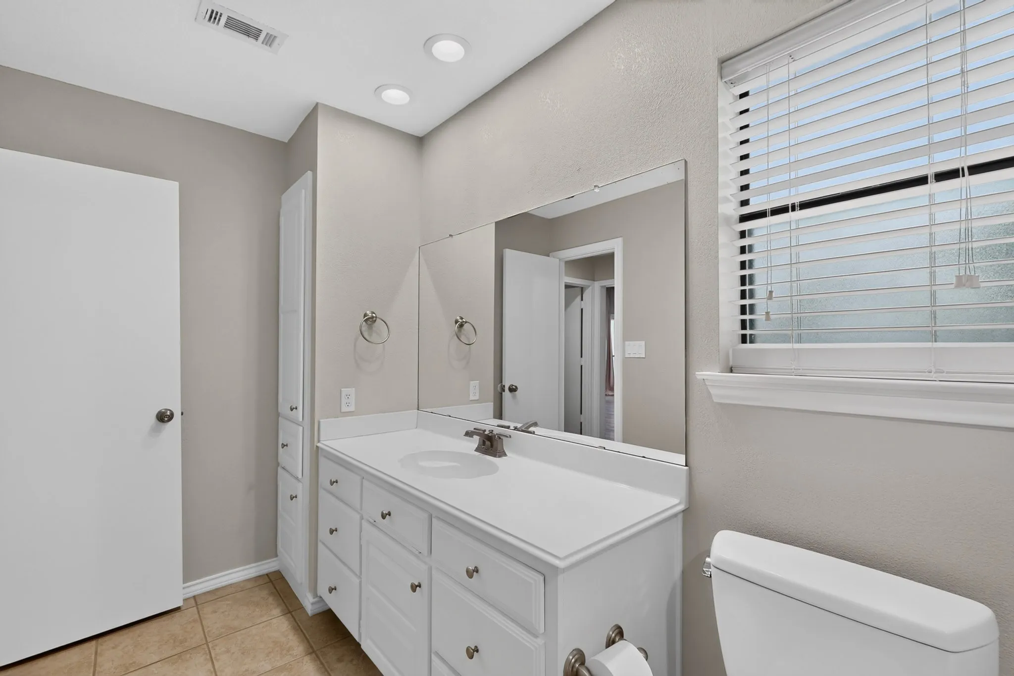 Bathroom featuring a white vanity with integrated sink, a large mirror, recessed lighting, and a built-in linen cabinet
