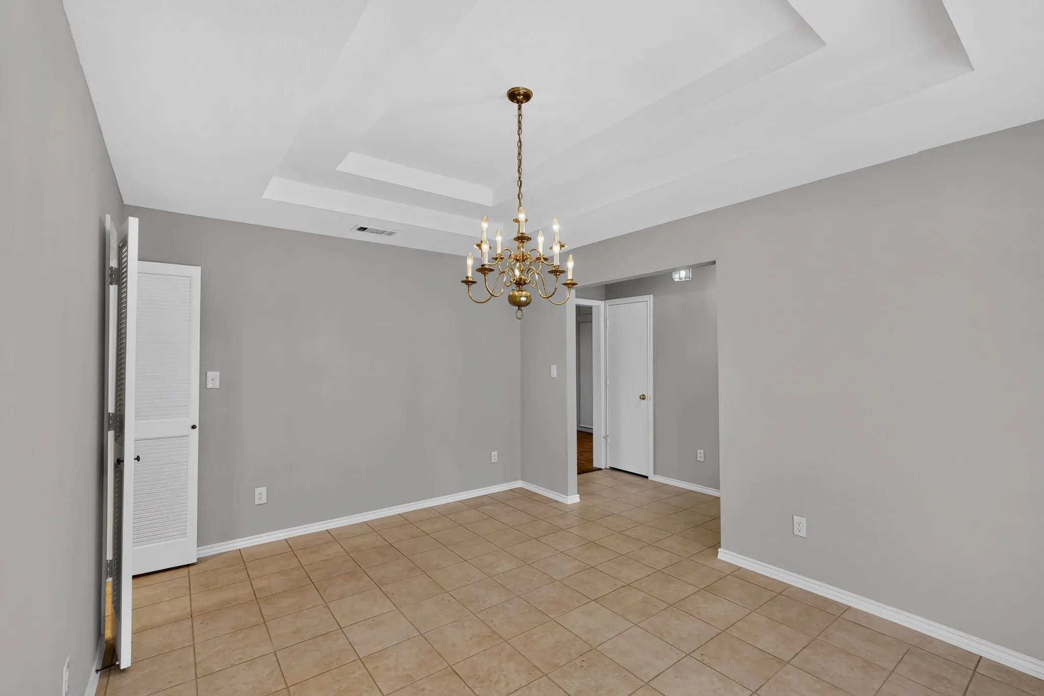 Recessed tray ceiling with a brass chandelier, tile flooring, and light gray wall paint