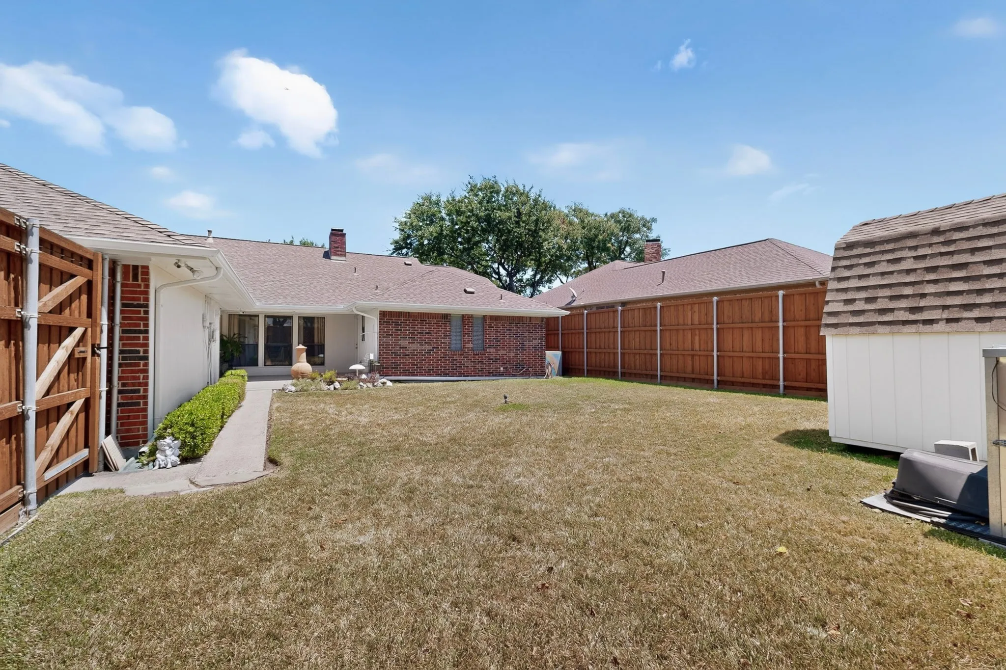 Expansive backyard featuring a privacy fence, brick exterior, and a detached storage shed