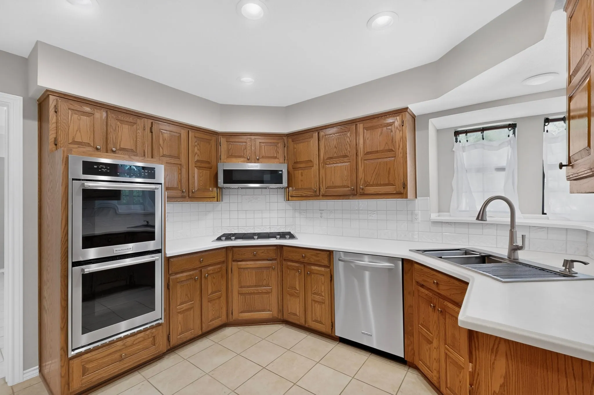 Chef's kitchen featuring warm wood cabinetry with raised-panel doors, stainless steel dual wall ovens, gas cooktop, and a large island with white quartz countertop and undermount sink