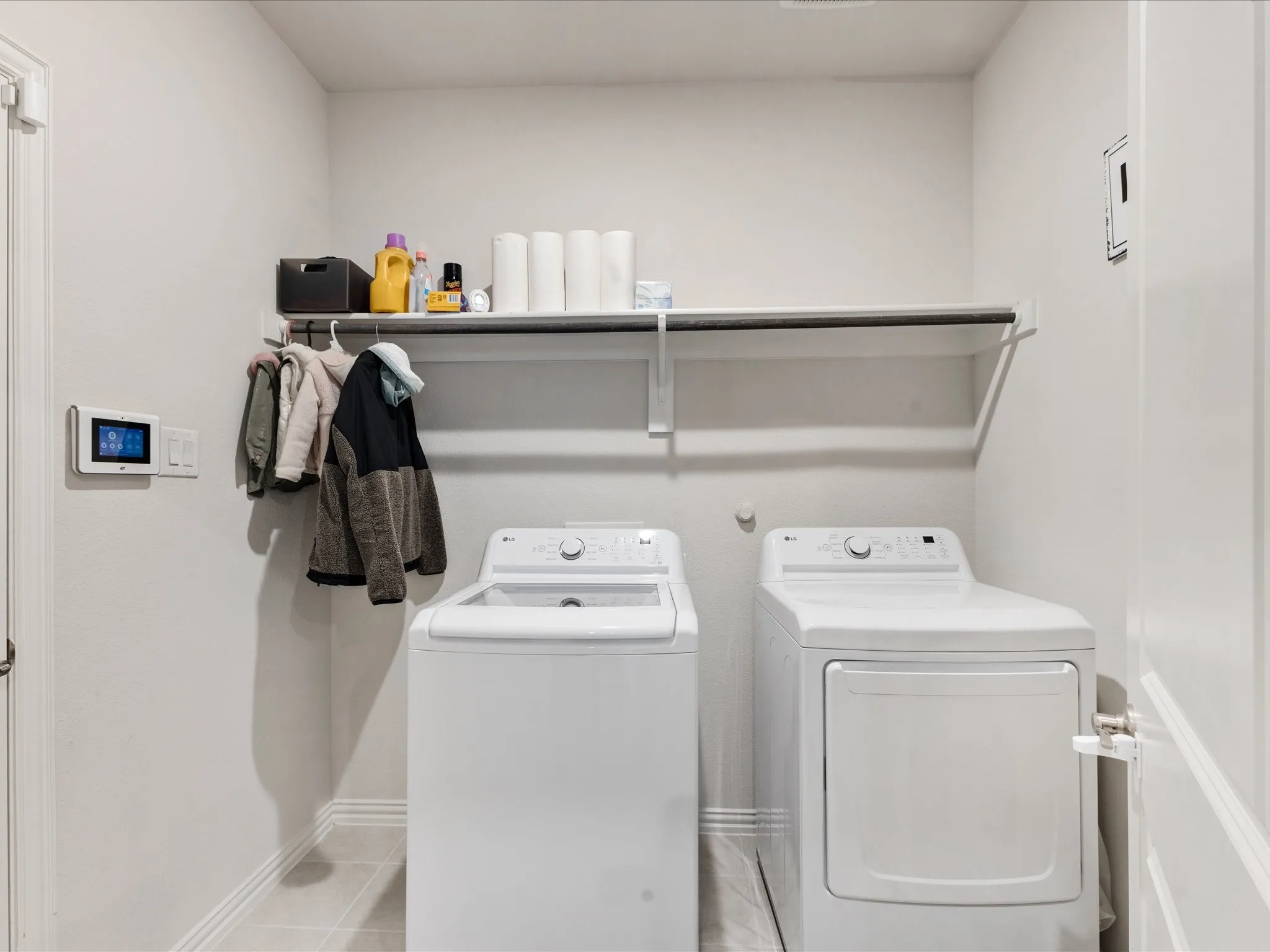 Dedicated laundry room featuring side-by-side washer and dryer units, overhead storage shelving with organizational accessories, digital temperature control, and neutral finishes throughout