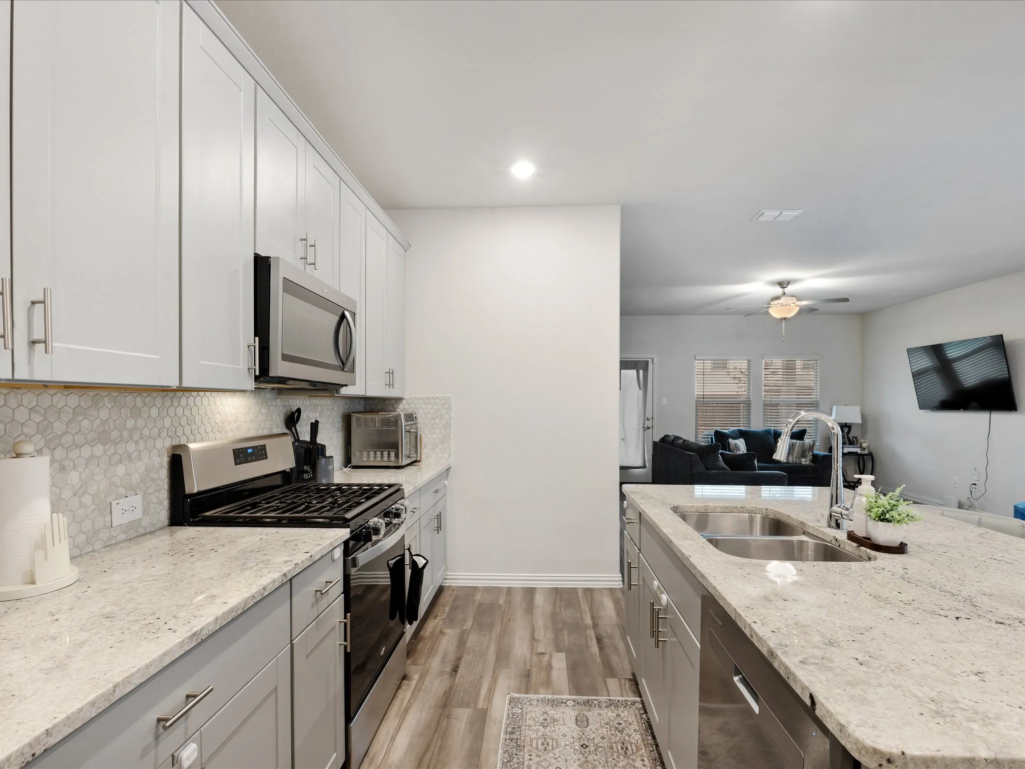 Kitchen featuring stainless steel appliances, light-toned cabinetry, light-toned countertops, a tile backsplash, and wood-finish flooring