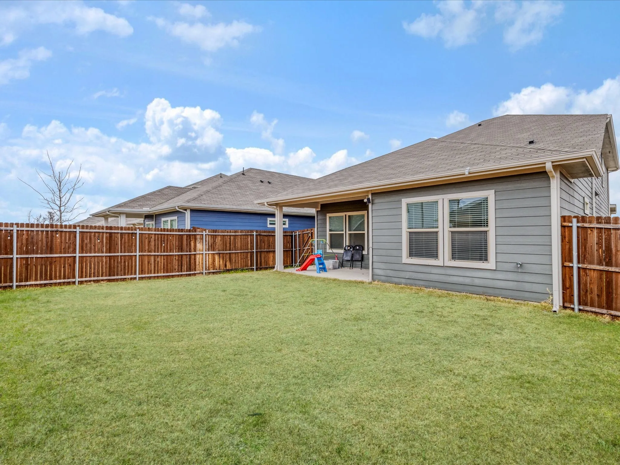Expansive grassy yard with a wood fence, concrete patio, and gray horizontal siding