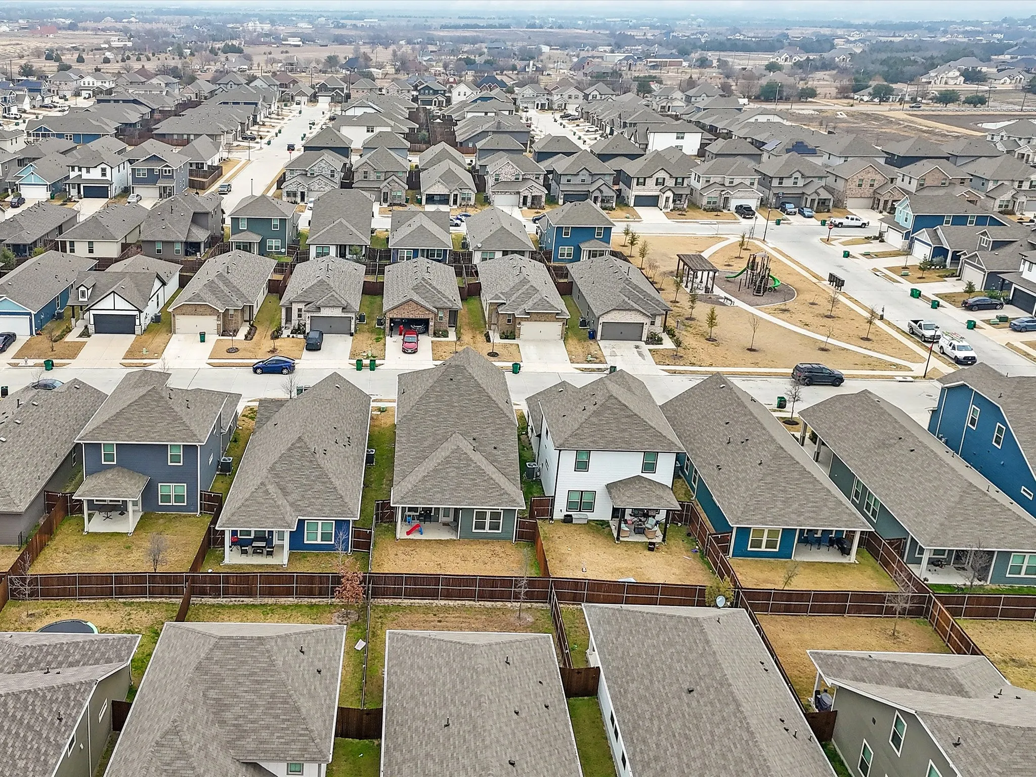 Aerial view showcasing a newly constructed residential community featuring multiple homes with varied exterior finishes including blue and gray siding, asphalt shingle roofing, and manicured front landscaping with young trees and defined lot lines
