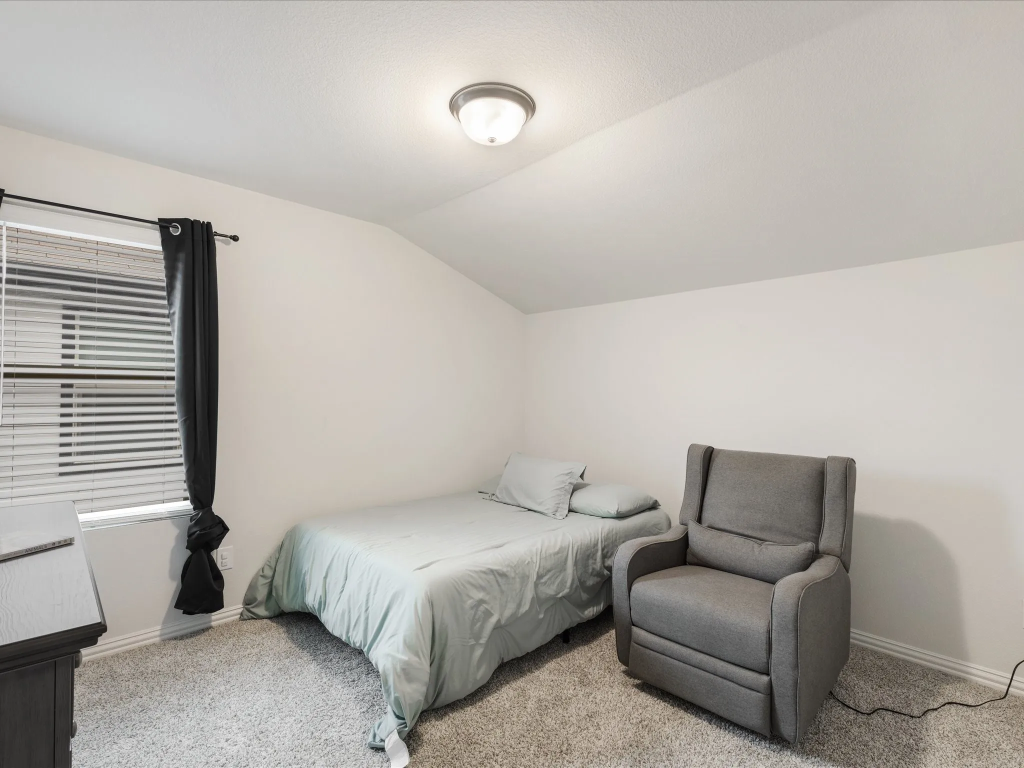 Angled ceiling lines with a flush-mount ceiling light fixture, window with blinds, and light gray carpet flooring