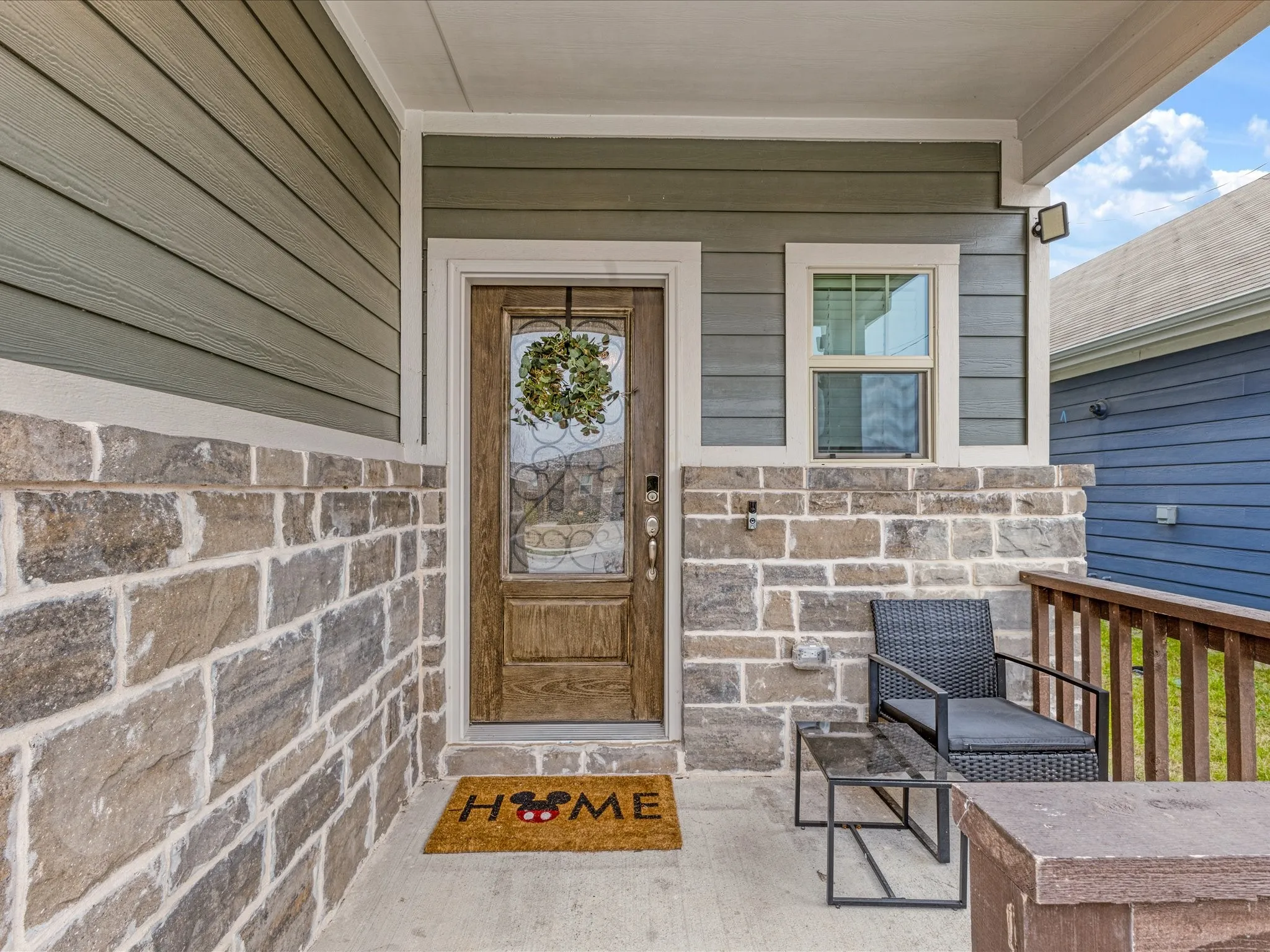 Front entrance featuring a paneled wood-finish door with decorative glass, stone veneer accents, horizontal siding, and a concrete porch