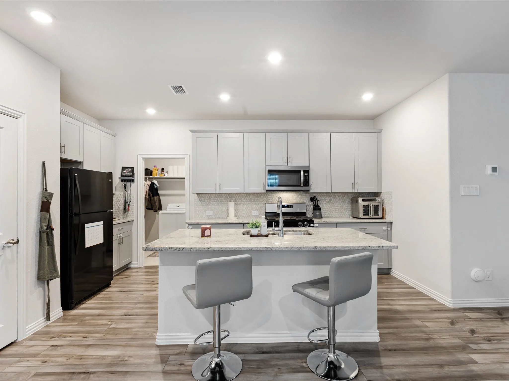 Modern kitchen featuring white cabinetry, stainless steel appliances, quartz countertops, a waterfall-edge island with seating for two, and wood-finish flooring throughout