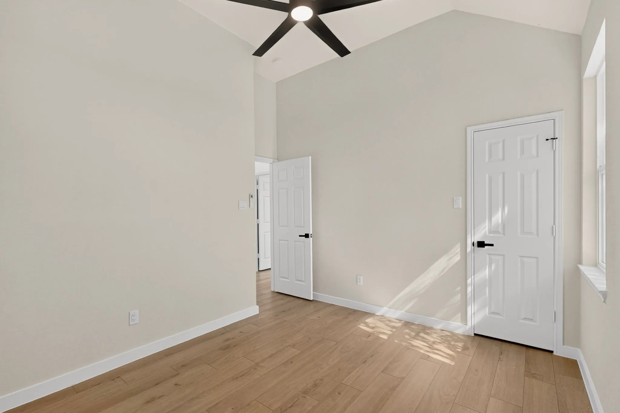 Bright and spacious bedroom featuring soaring vaulted ceilings with contemporary ceiling fan, warm wood-finish flooring throughout, and multiple white six-panel doors