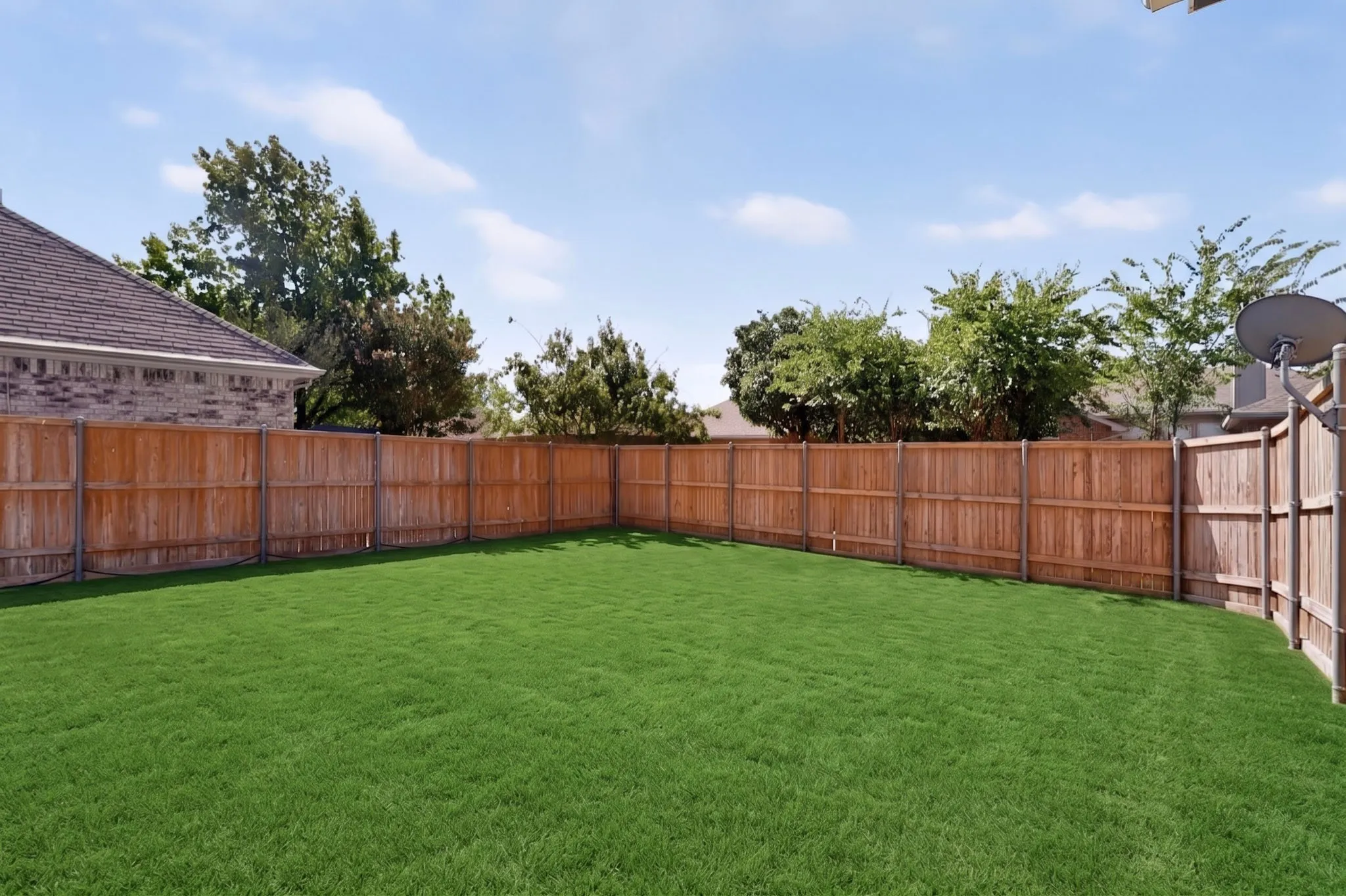Expansive backyard with a lush lawn, featuring a wood privacy fence and mature trees