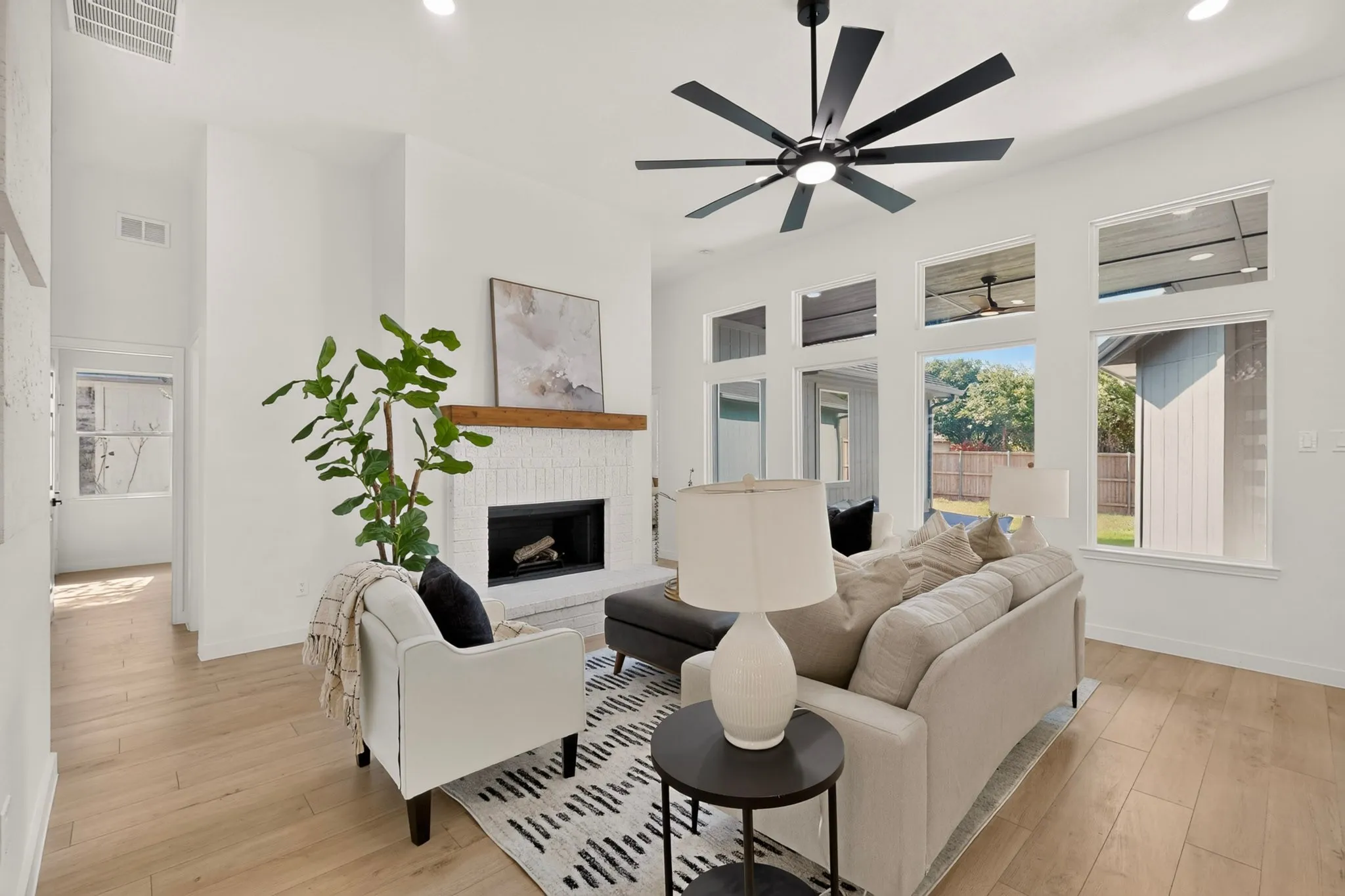 Bright living area featuring wood-finish flooring, a white brick fireplace with a wood mantle, recessed lighting, and a contemporary ceiling fan