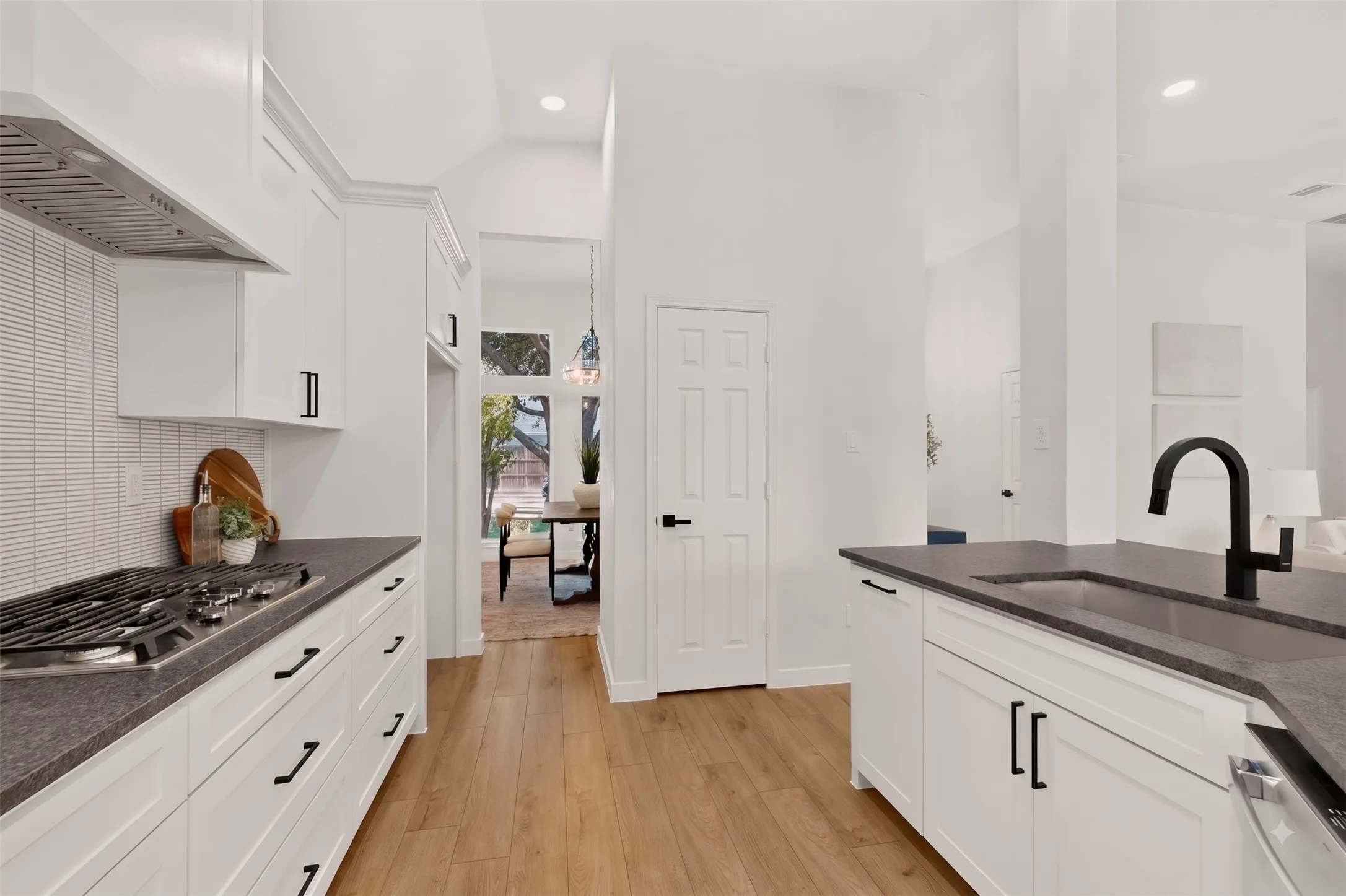 Kitchen featuring white cabinetry with dark hardware, dark countertops, a built-in gas range with vent hood, and wood-finish flooring
