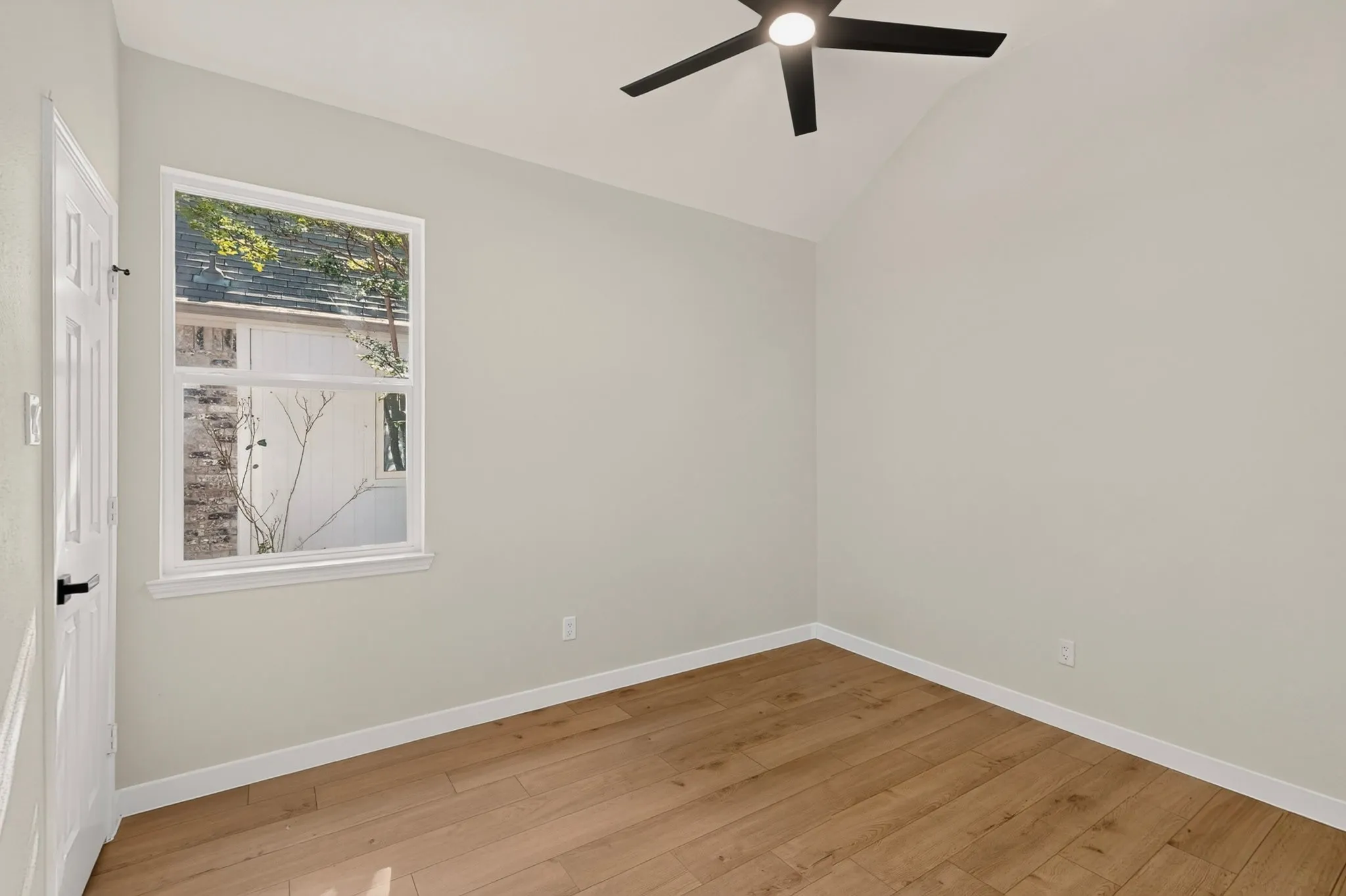 Angled ceiling, wood-finish flooring, white trim, modern ceiling fan, single-hung window