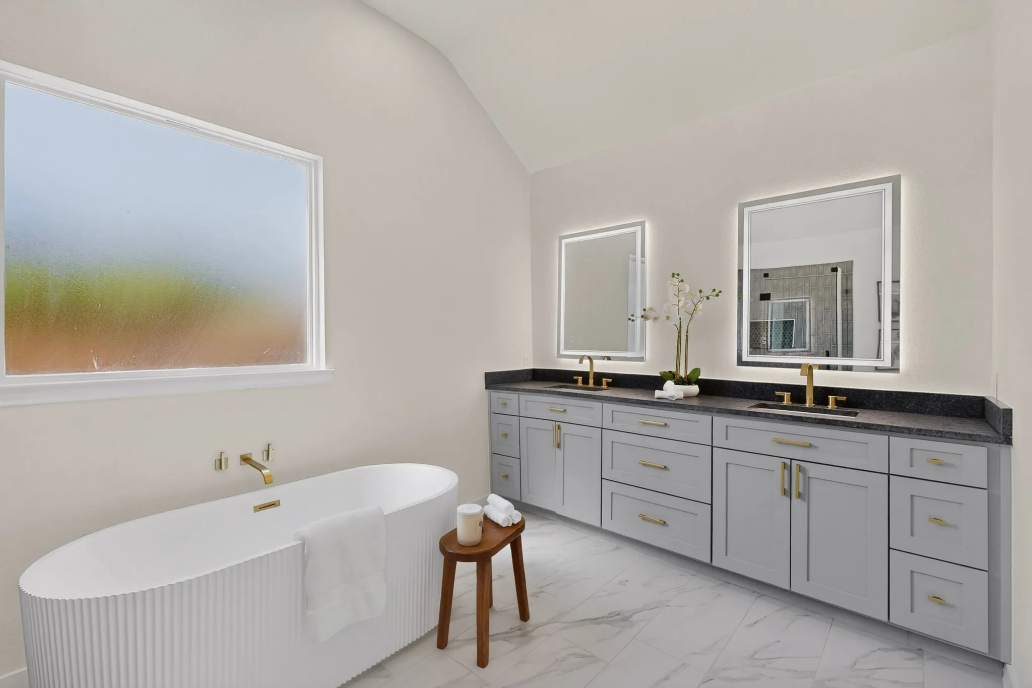 Freestanding soaking tub with wall-mounted brass faucet, dual vanity with undermount sinks, and illuminated mirrors