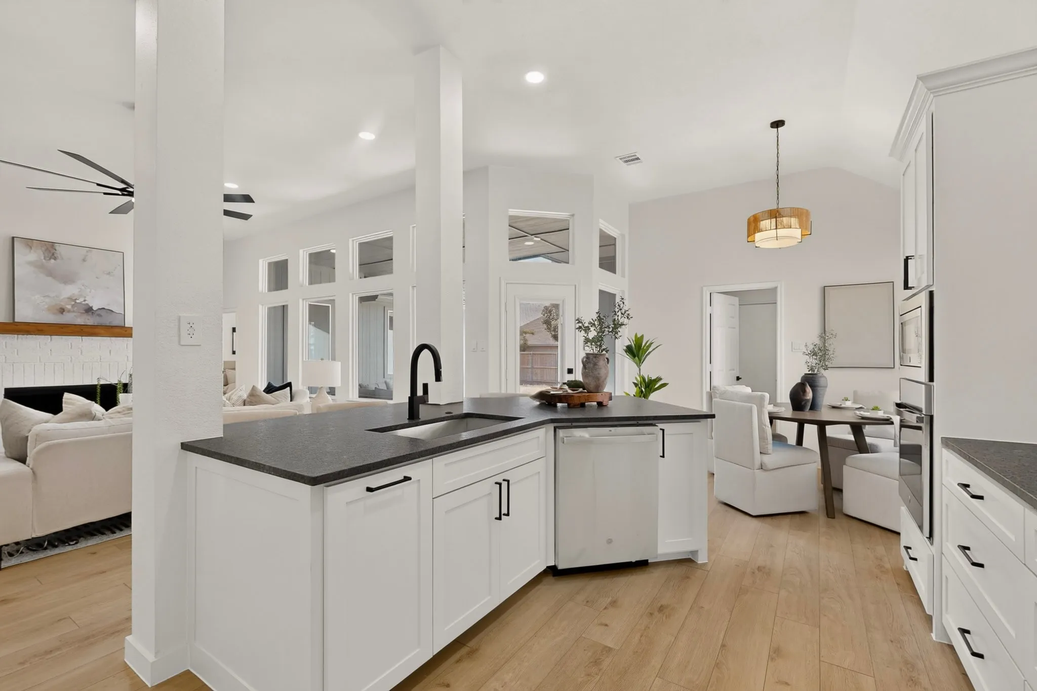 Kitchen island with a built-in sink and matte black faucet, dark countertops, white cabinetry with black hardware, wood-finish flooring, and a vaulted ceiling