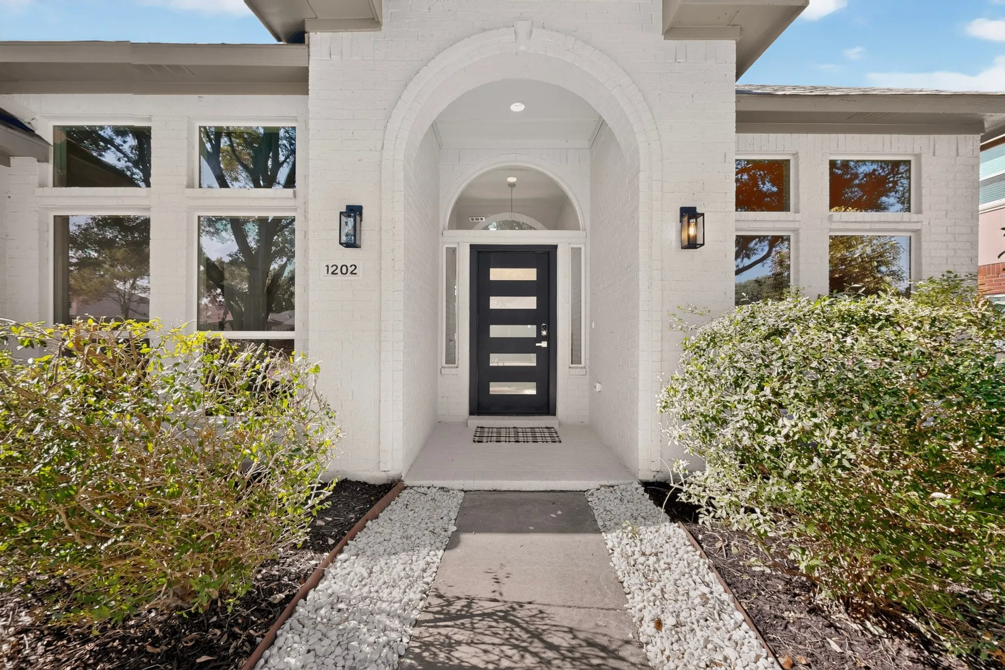White brick exterior with an arched entryway, a black front door featuring horizontal lites, and large windows