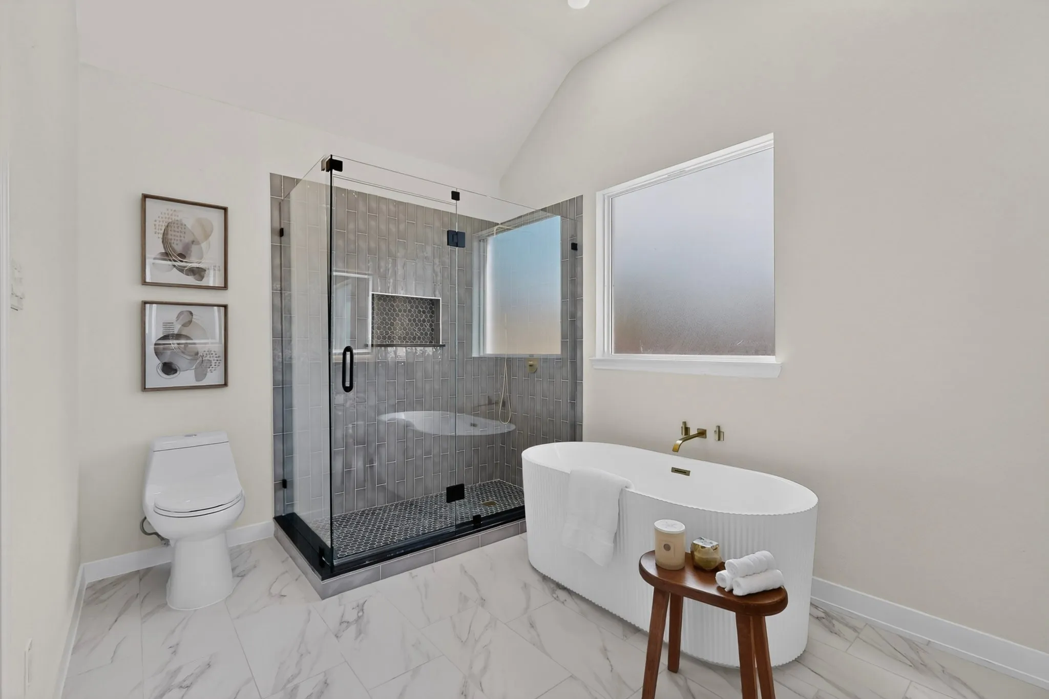 Freestanding soaking tub with wall-mounted faucet, glass-enclosed shower with tile surround, and marble-look tile flooring