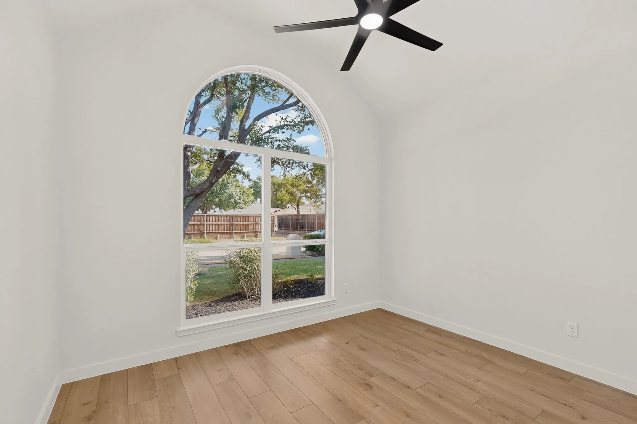 Arched window with white trim, wood-finish flooring, and a black ceiling fan