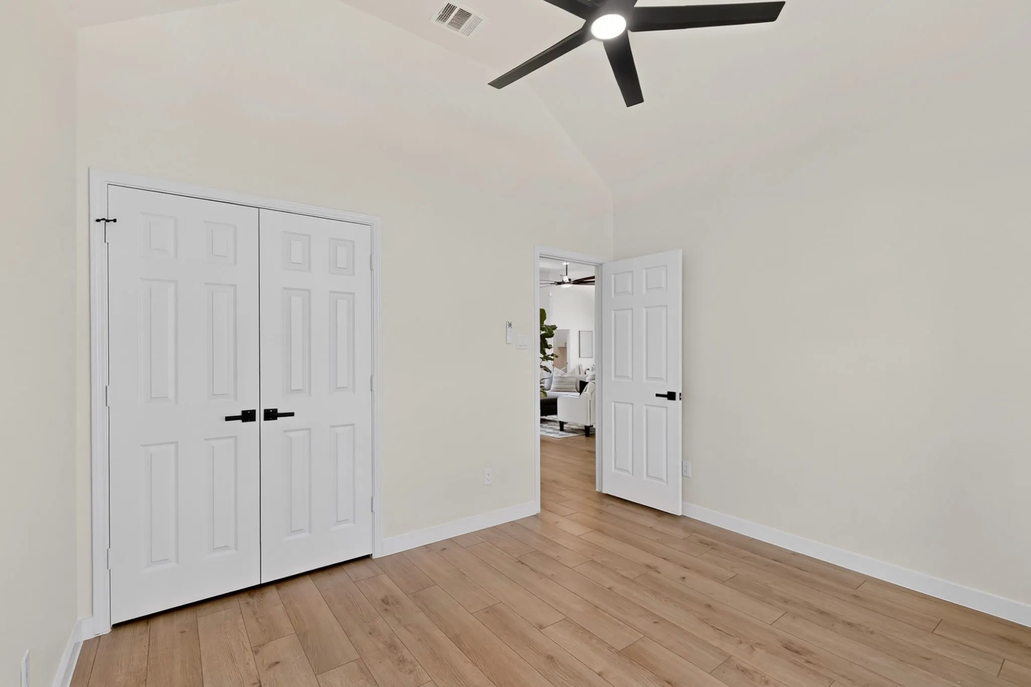 Vaulted ceiling with a black ceiling fan, light wood-finish flooring, white paneled doors, and white baseboards