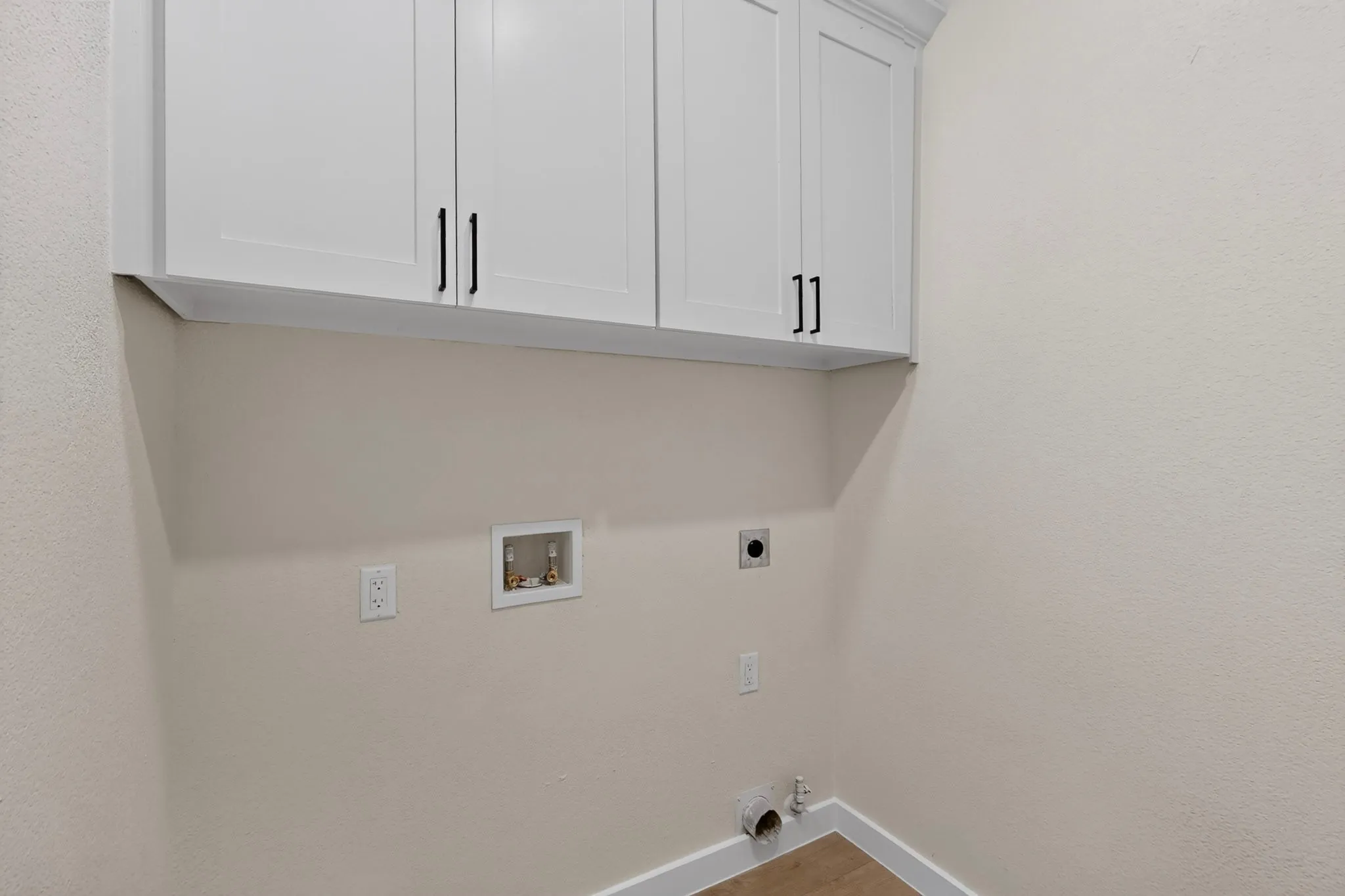 Dedicated laundry room featuring white shaker-style cabinetry with brushed nickel hardware, neutral wall finishes, and practical utility outlets for appliance connections