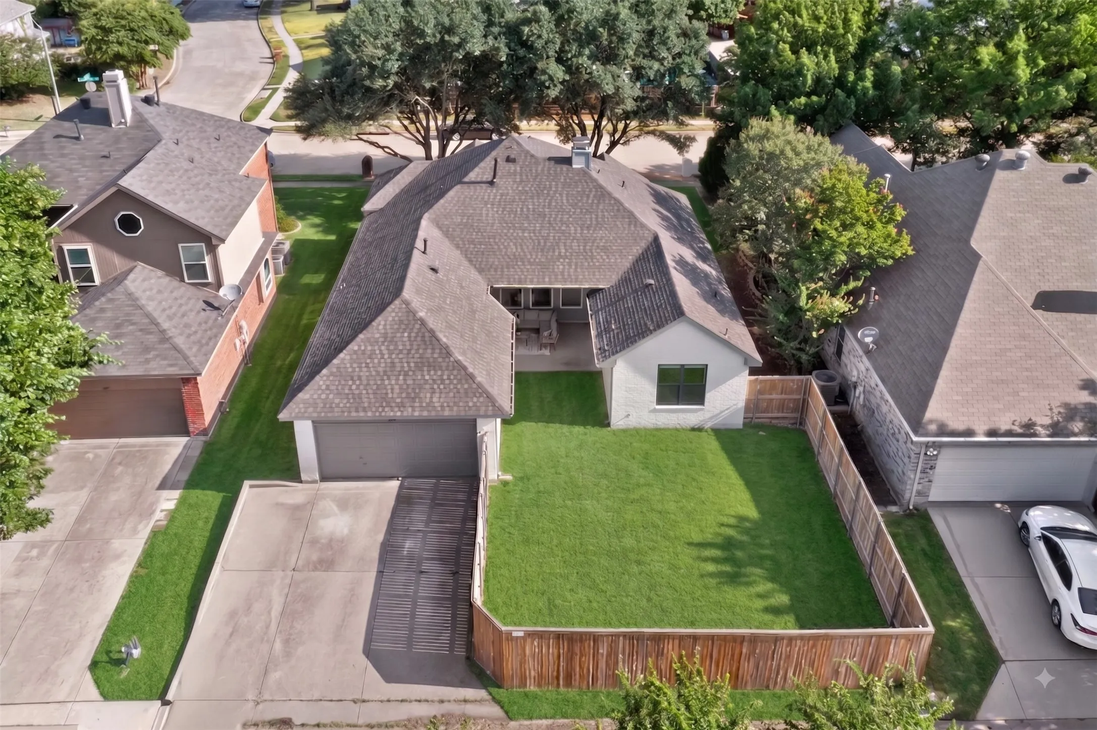 Fenced backyard with expansive lawn, concrete patio, and attached two-car garage