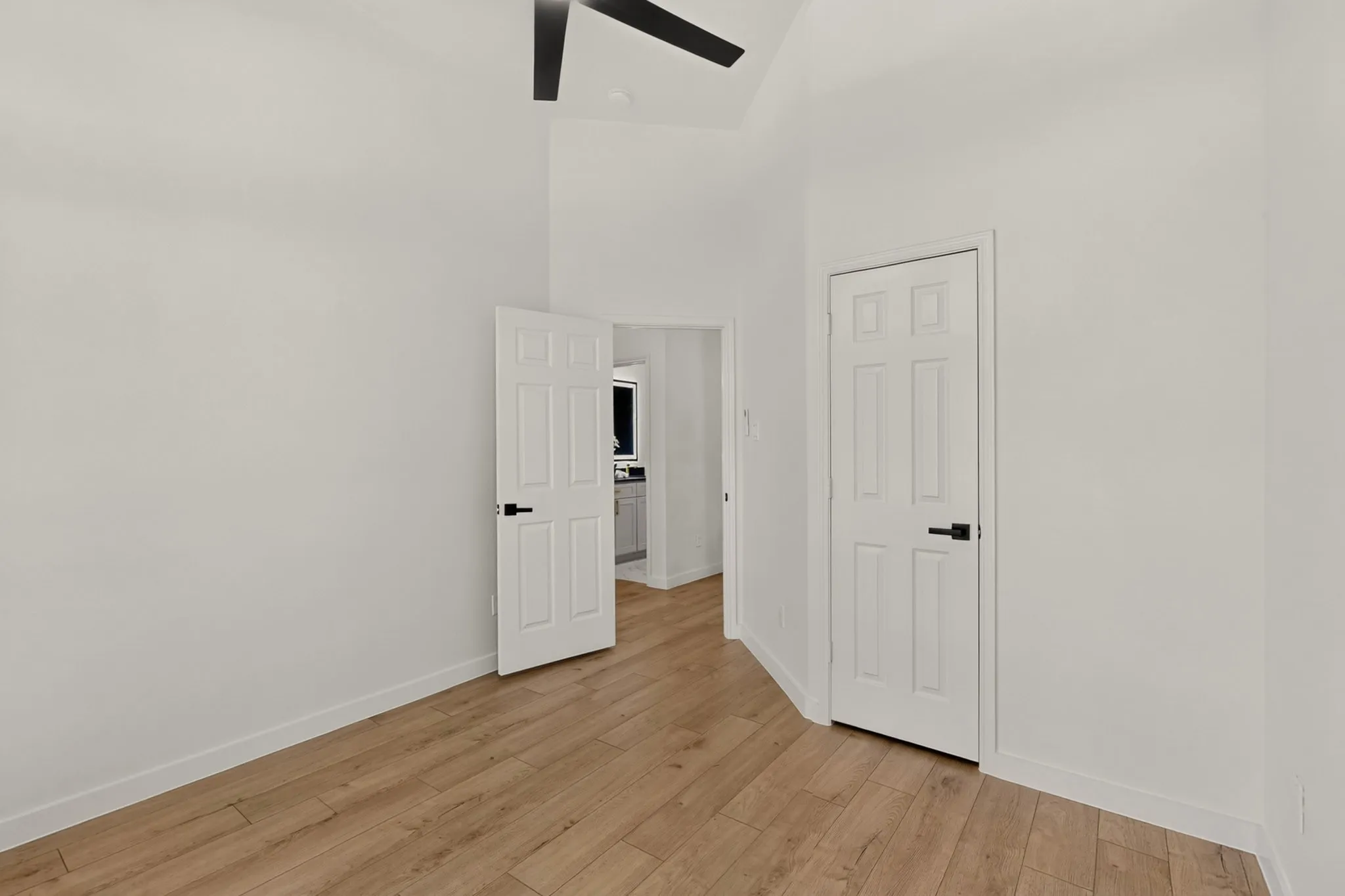 Vaulted ceiling, wood-finish flooring, paneled interior doors, and a ceiling fan